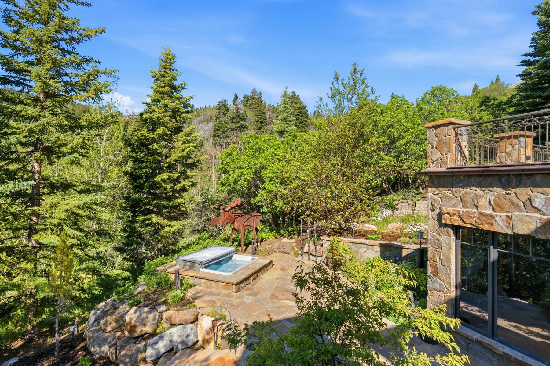 Outdoor patio featuring an integrated hot tub with stone surround, complemented by a natural stone retaining wall and extensive mature trees