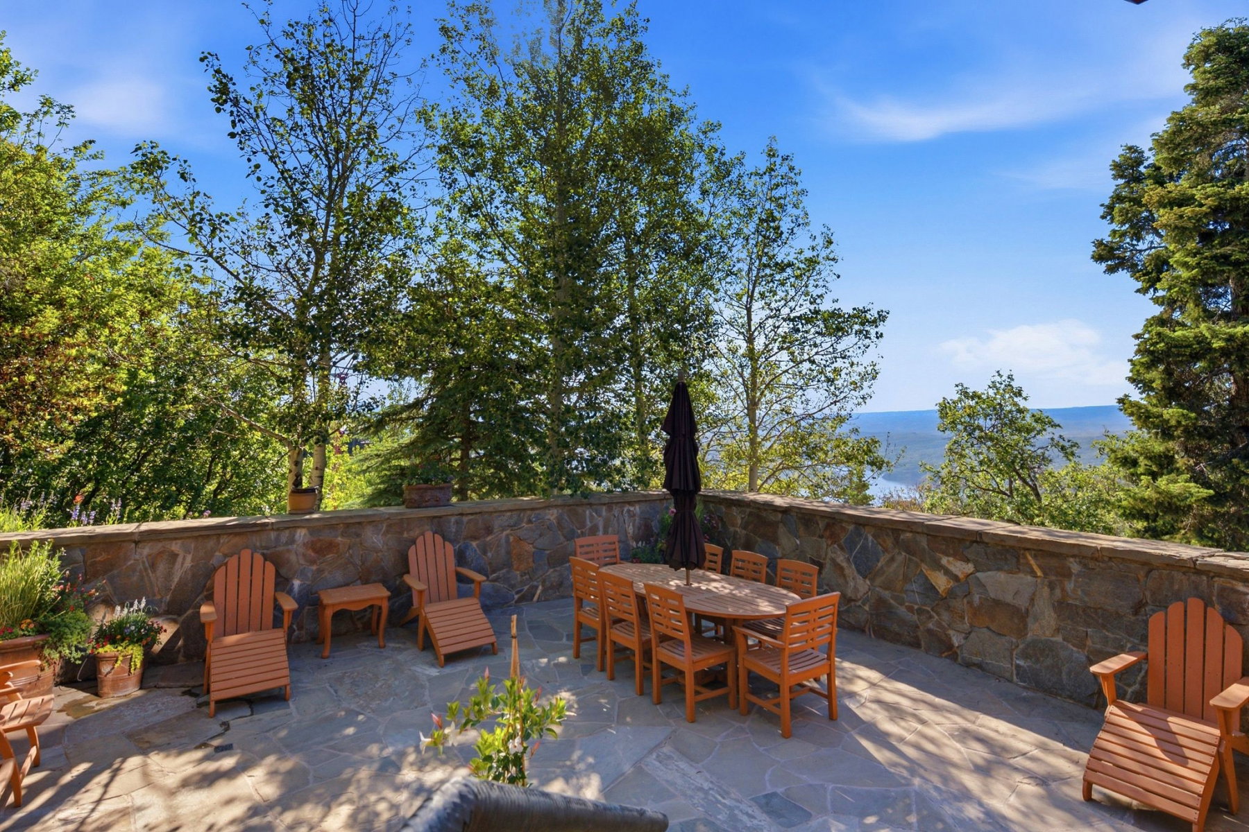 Expansive stone patio featuring a natural stone wall, mature trees, and a distant water backdrop