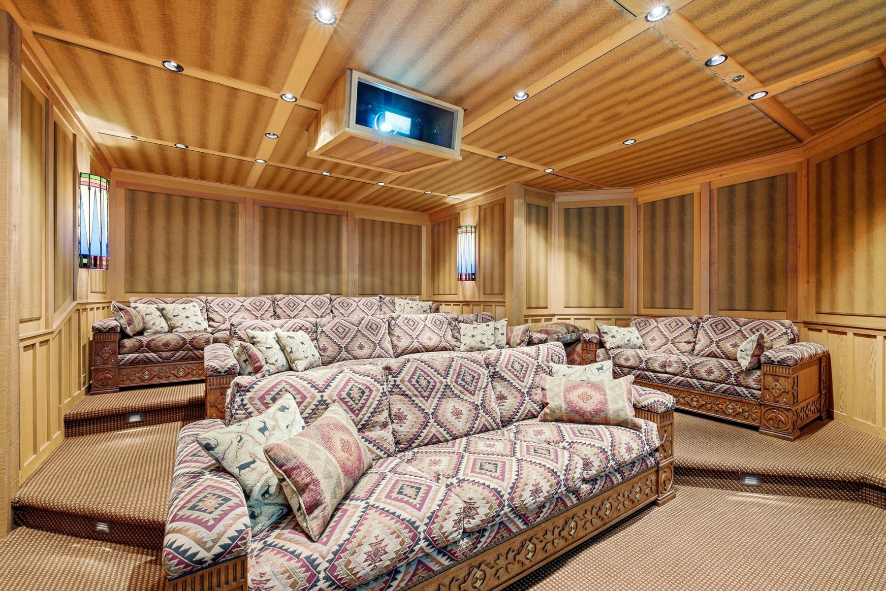 Dedicated media room featuring tiered seating, wood-paneled walls, recessed ceiling lighting, and a built-in projector with screen