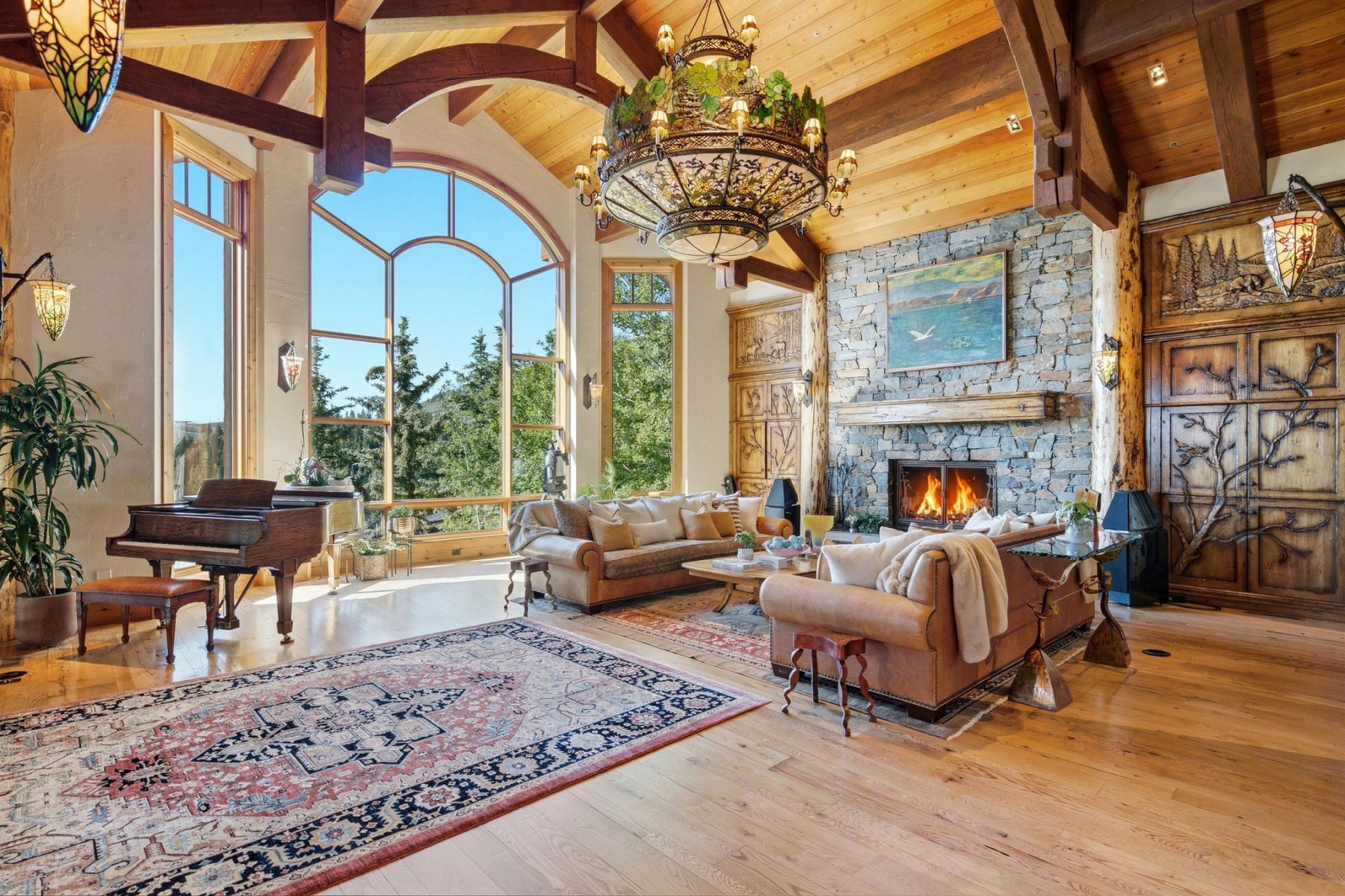 Grand living area featuring vaulted ceilings with exposed wood beams, a stone-clad fireplace with a wood mantle, and expansive arched windows