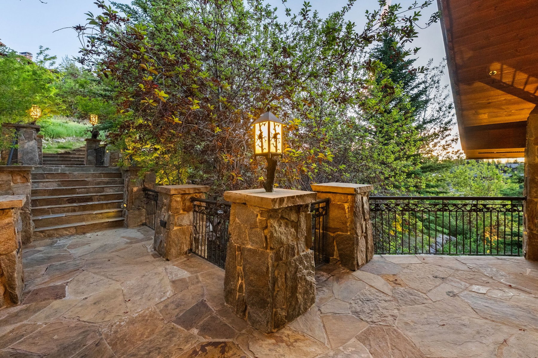 Stone patio with flagstone flooring, solid stone pillars, decorative exterior lighting, and an ornate metal railing