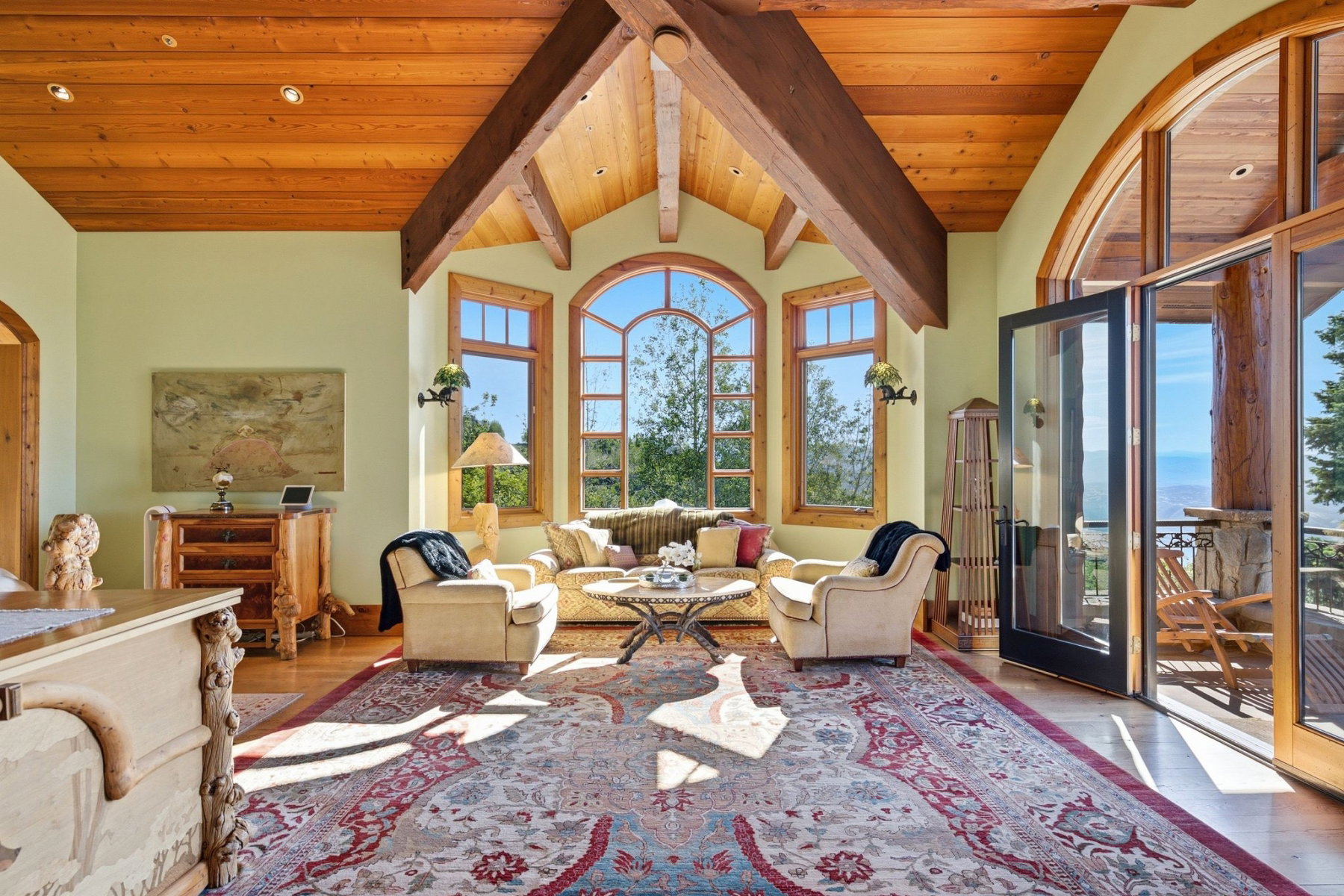 Bright room featuring a vaulted wood-paneled ceiling with exposed wood beams, arched windows, light-colored walls, wood-finish flooring, and a glass-paneled double door opening to an exterior space