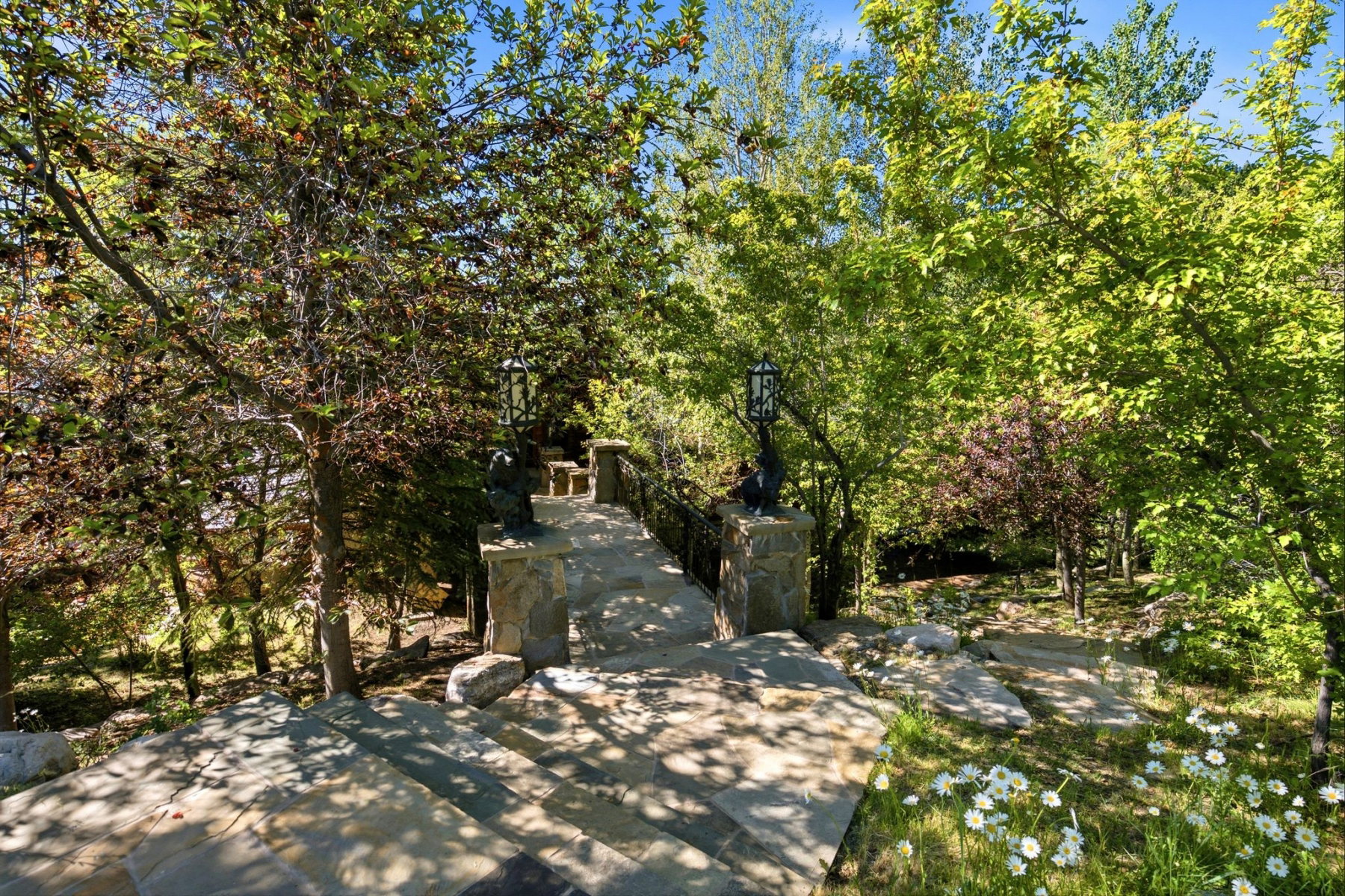 Terraced stone staircase featuring integrated stone posts with lanterns, surrounded by mature trees and natural landscaping