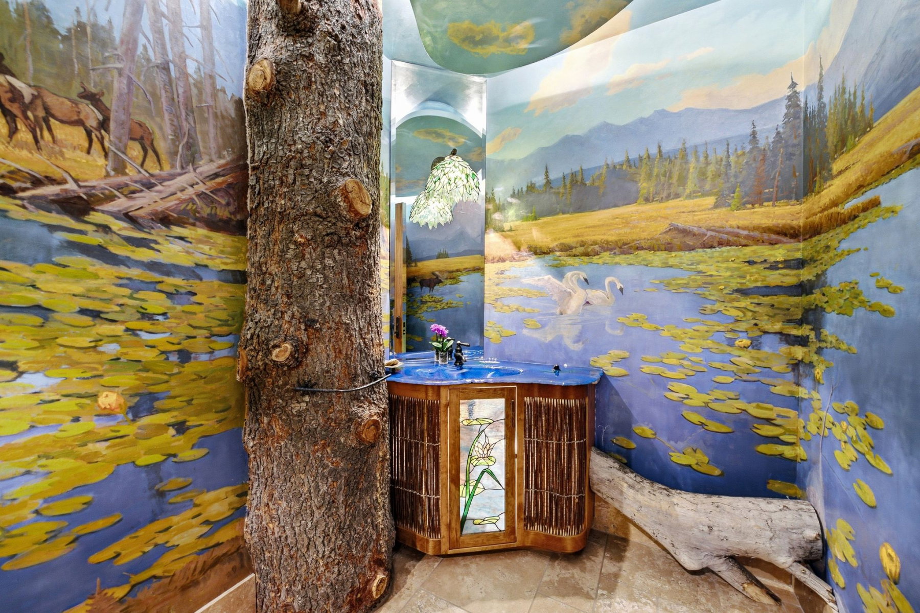 Bathroom featuring an integrated tree trunk, custom mural artwork, built-in wooden vanity with a blue countertop basin, and natural wood elements
