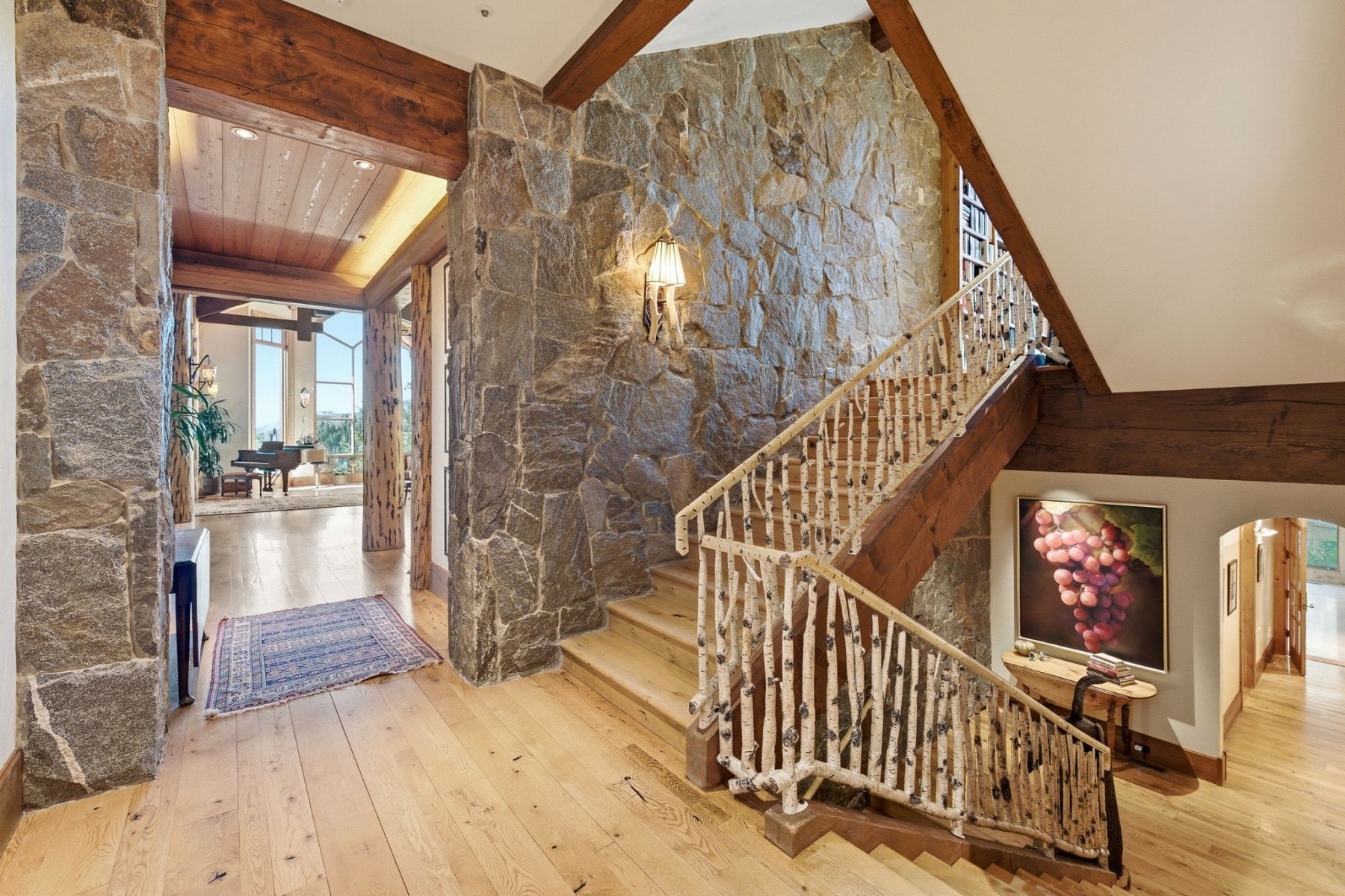 Stone-clad entryway featuring wood-finish flooring, exposed wood beams, and a natural branch staircase railing