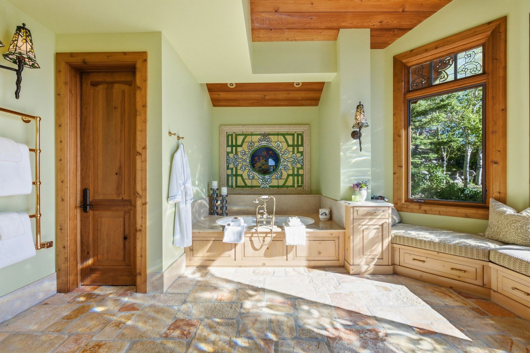 Bathroom featuring a built-in soaking tub, stone tile flooring, and a window seat with storage