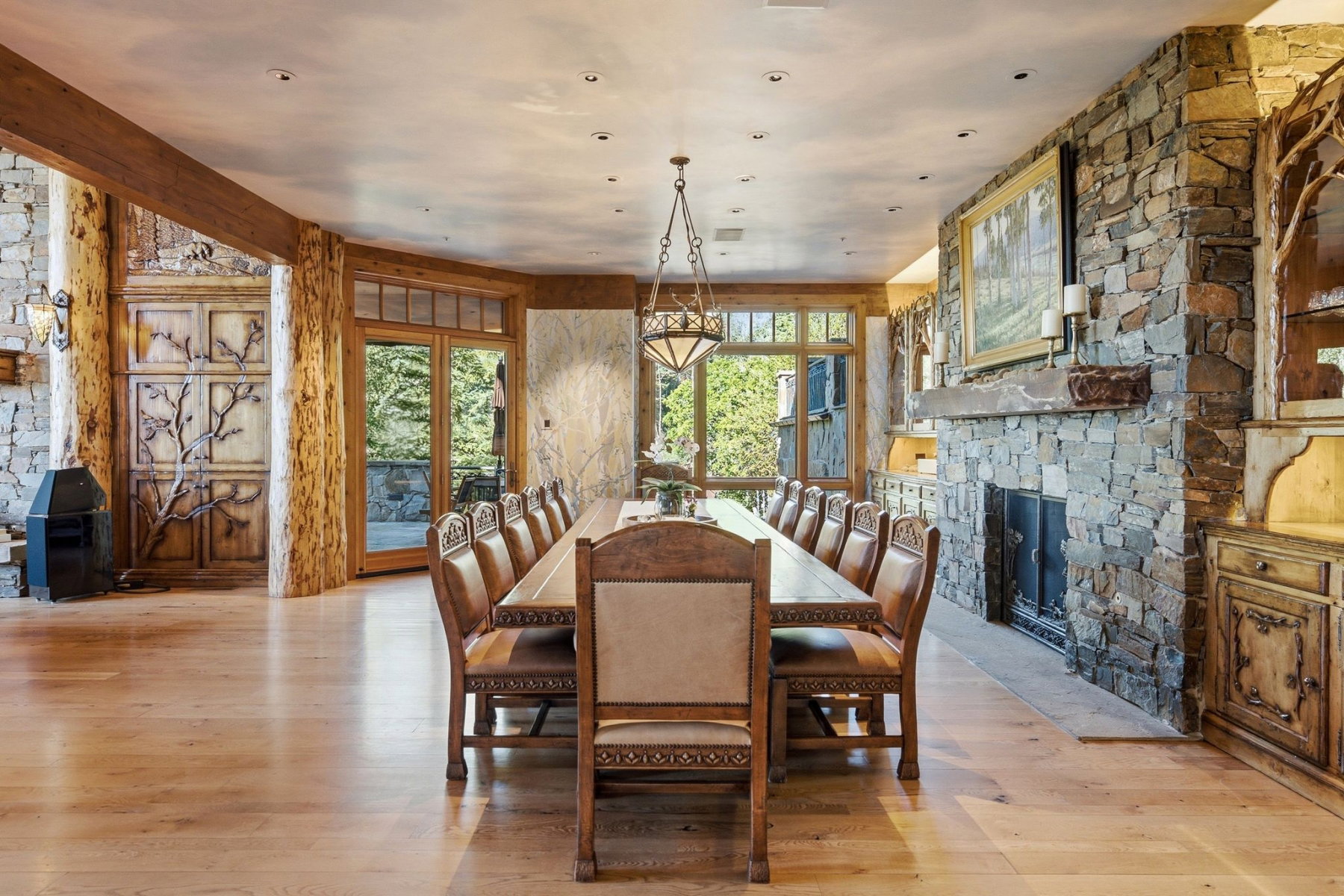 Spacious dining area featuring stone accent walls, natural wood-finish flooring, and a stone fireplace with a substantial mantel