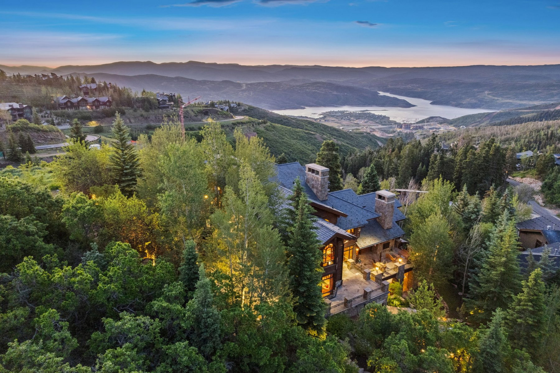 Hillside property featuring extensive tree coverage, a multi-level deck, stone chimneys, and a dark shingle roof