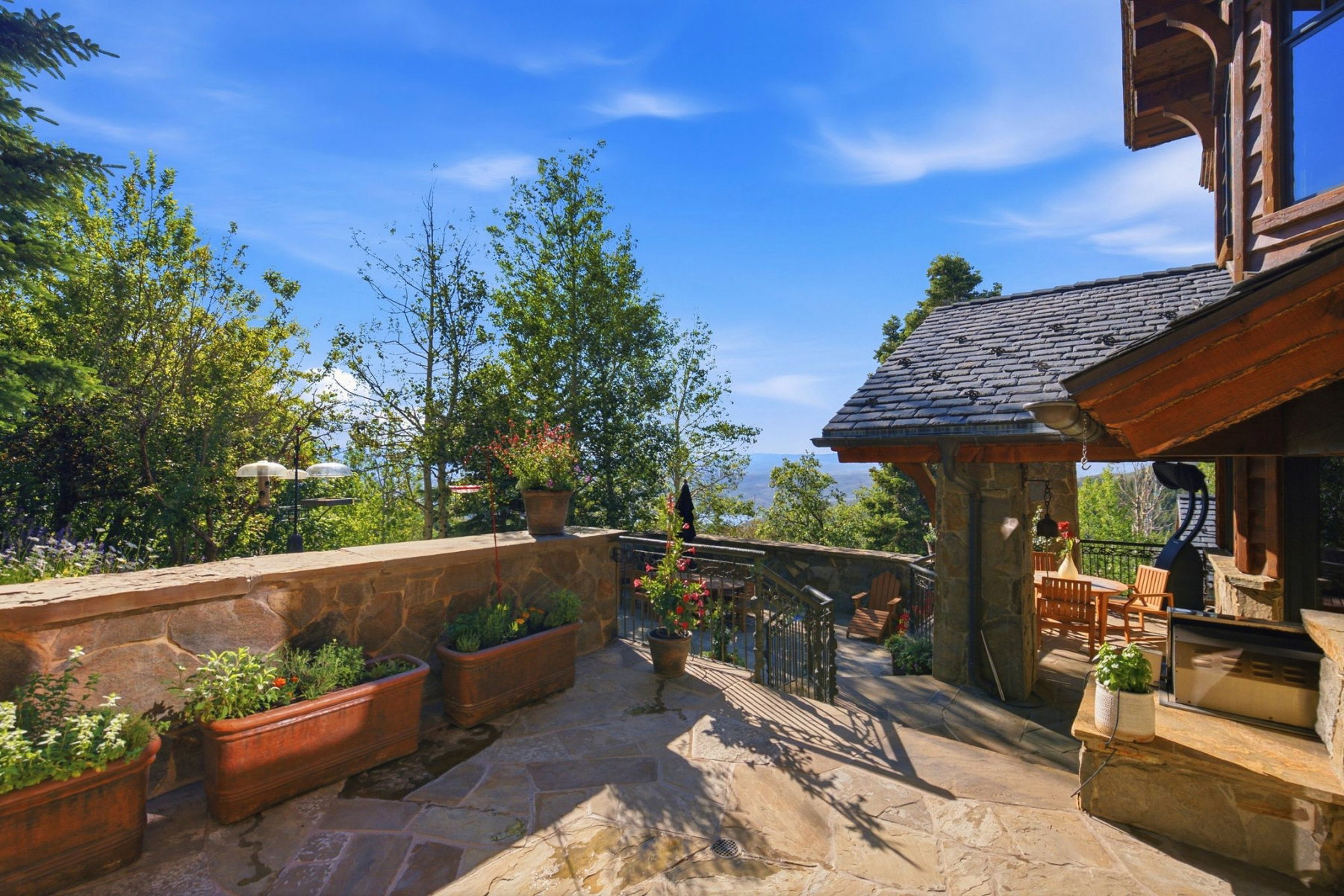 Outdoor stone patio with flagstone flooring, a stone retaining wall, and multiple planter boxes