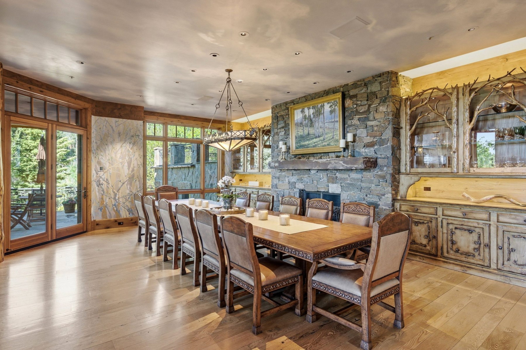 Spacious dining area featuring wood-finish flooring, a stone-clad fireplace with mantel, French doors opening to an outdoor patio, and custom built-in cabinetry with branch detailing