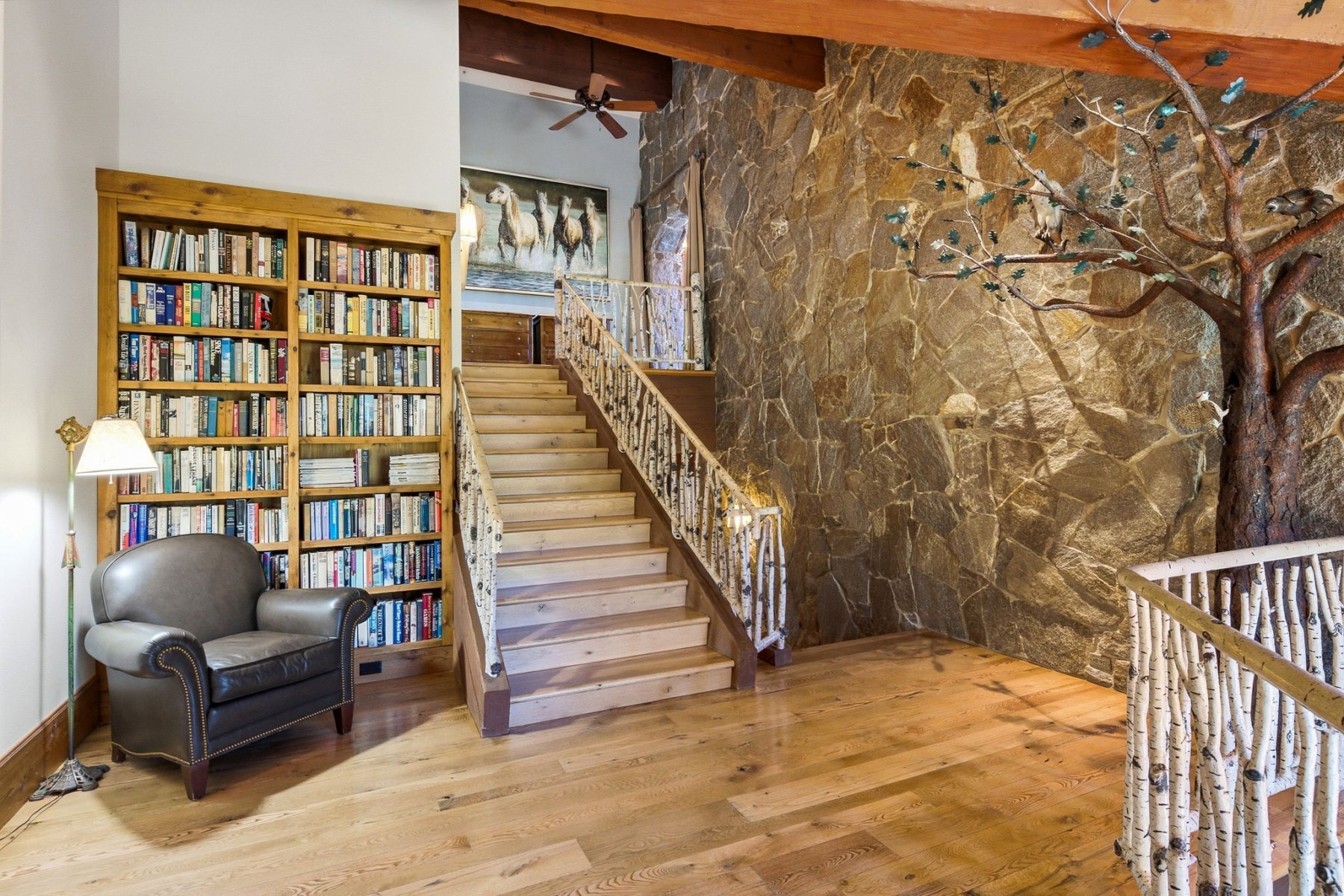 Hardwood flooring extends throughout this expansive space, featuring a stone accent wall with an integrated tree sculpture