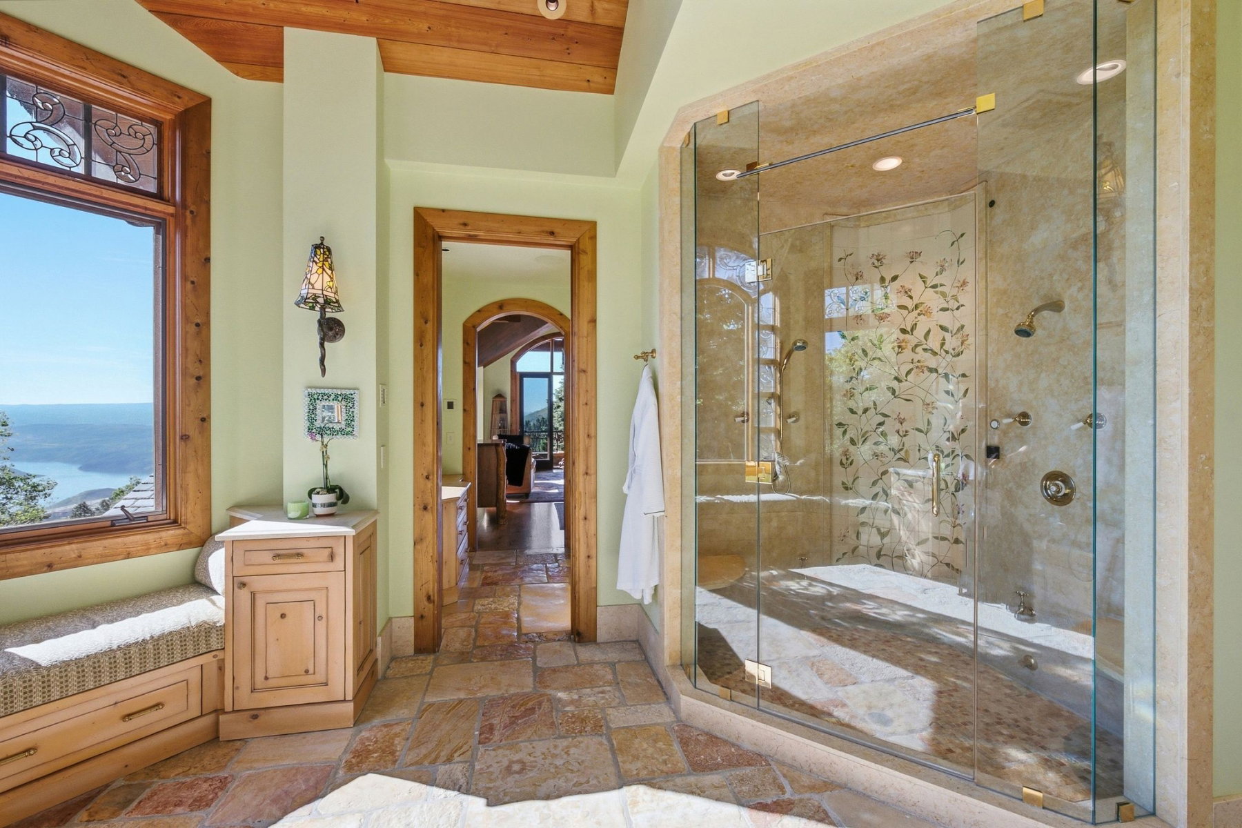 Spacious bathroom featuring a large glass-enclosed shower with multiple showerheads, stone-finish walls, and decorative glass panels