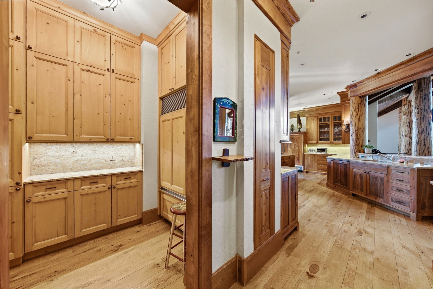 Custom wood cabinetry with under-cabinet lighting, natural wood-finish flooring, and a stone backsplash