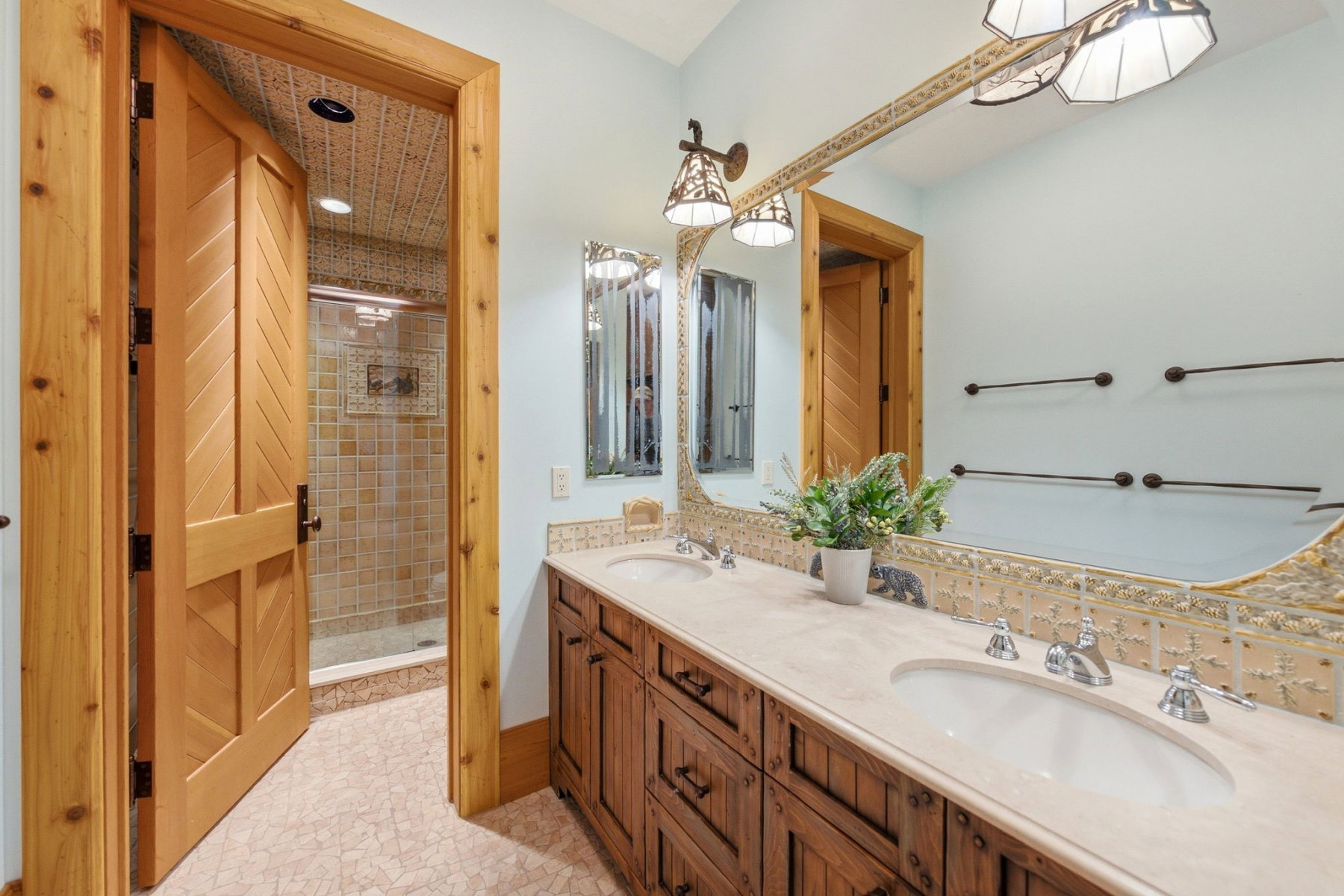Bathroom featuring a dual vanity with light-toned countertops and integrated sinks, custom wood cabinetry, an ornate framed mirror, and decorative wall sconces