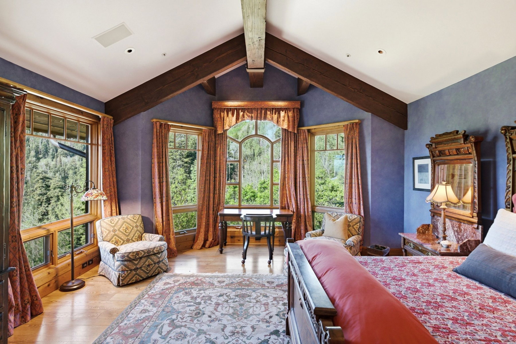 Vaulted ceiling with exposed wood beams, extensive natural light from multiple wood-framed windows, and light wood-finish flooring
