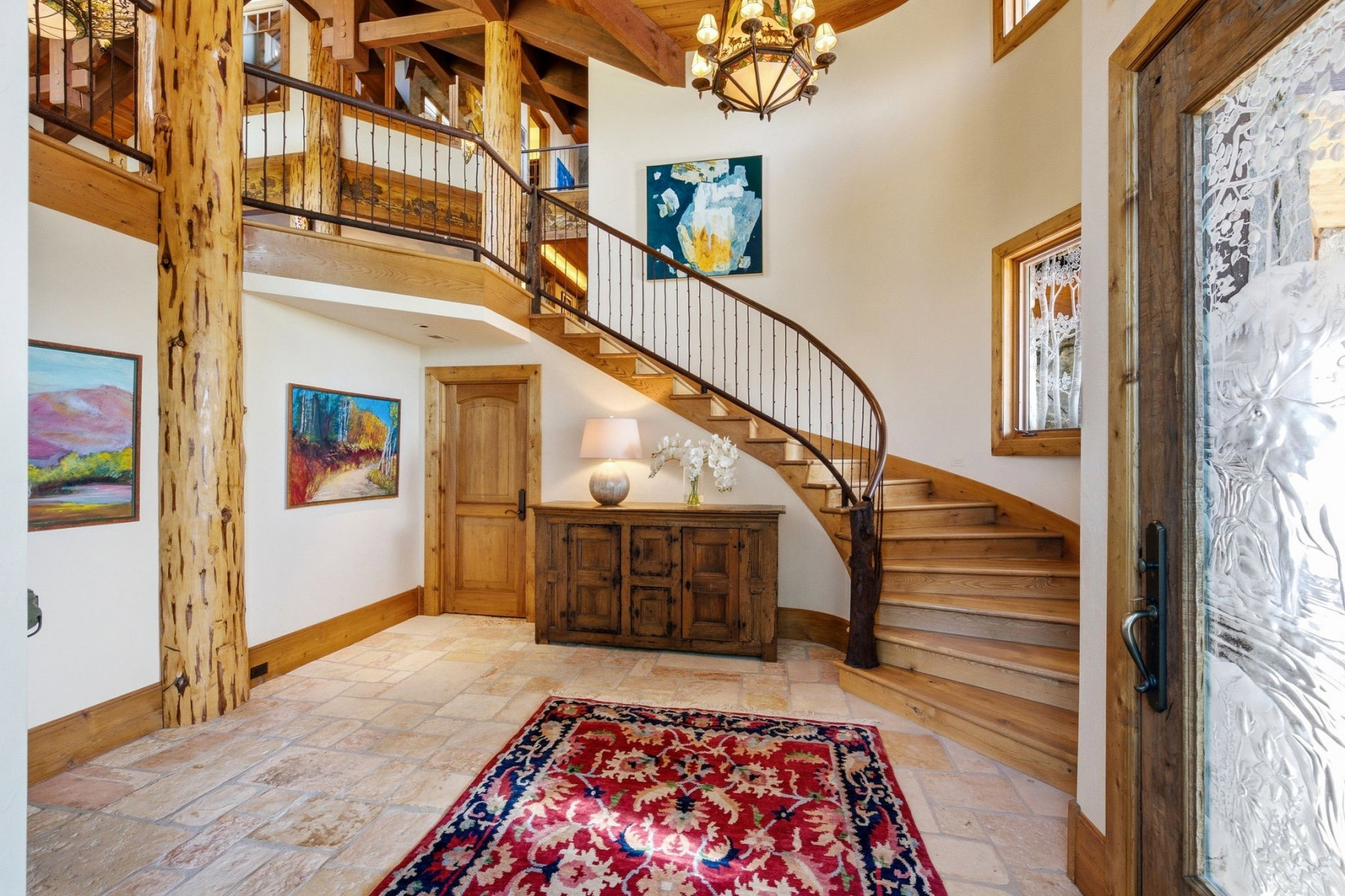 Grand entryway featuring a curved wood staircase with wrought iron balusters, natural wood structural beams, and stone tile flooring