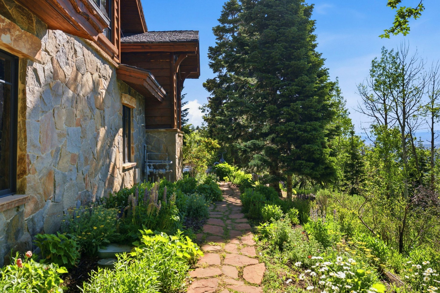 Stone facade with dark-framed windows and wood trim, featuring a flagstone pathway bordered by established landscaping