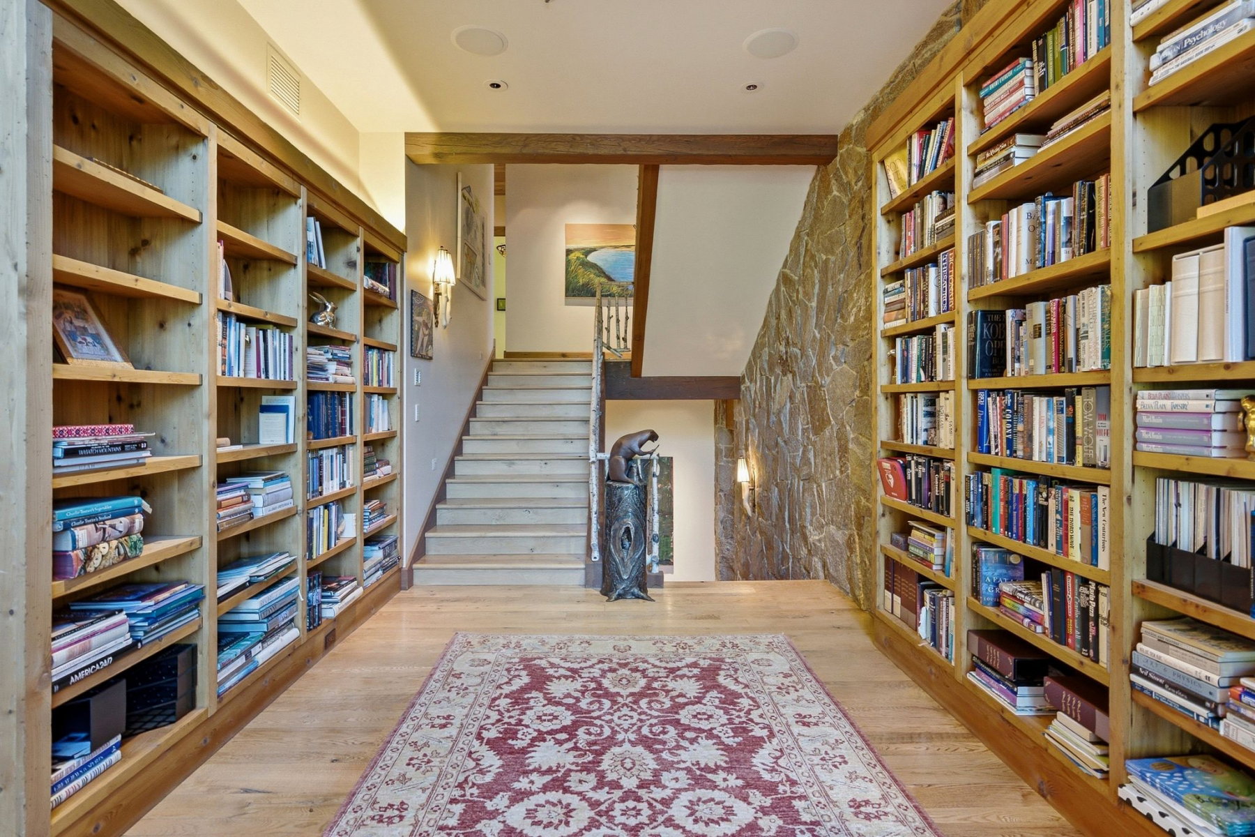Extensive built-in wood shelving units flank a wood-finish flooring area with a centrally placed area rug