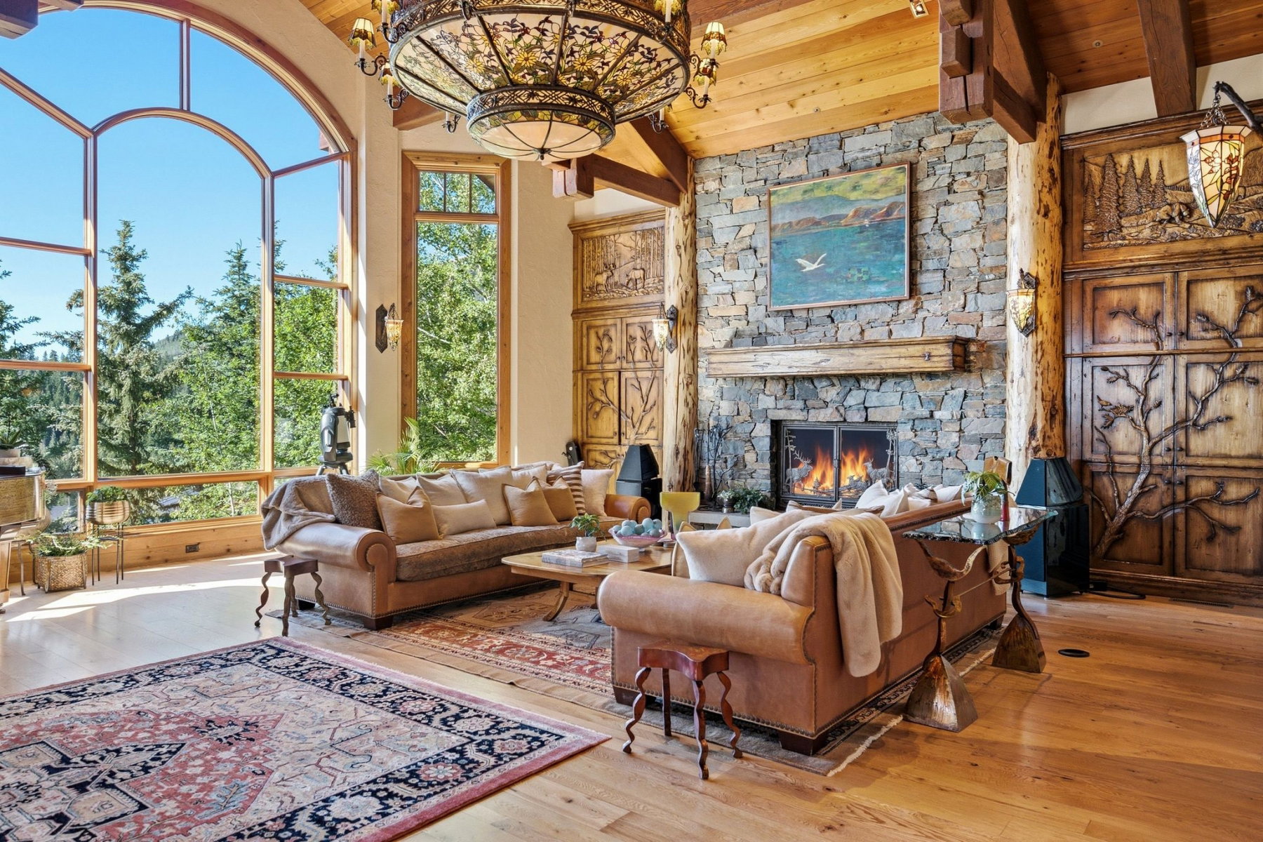 Great room featuring a floor-to-ceiling arched window, a stone fireplace with a wood mantle, wood-finish flooring, exposed wood beams, and built-in decorative wood panels