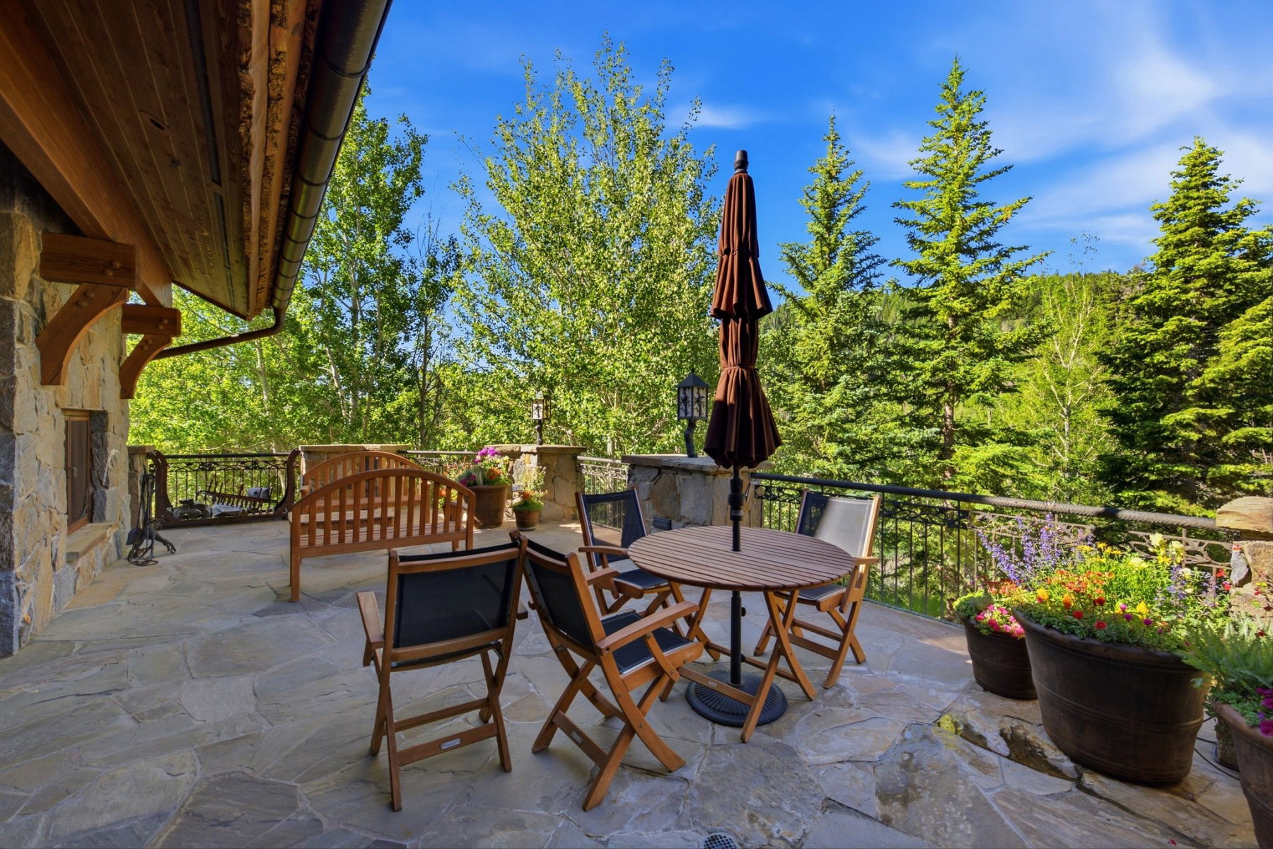 Expansive stone patio featuring a stone exterior wall, a wrought iron railing, and a tongue-and-groove wood ceiling with exposed beams