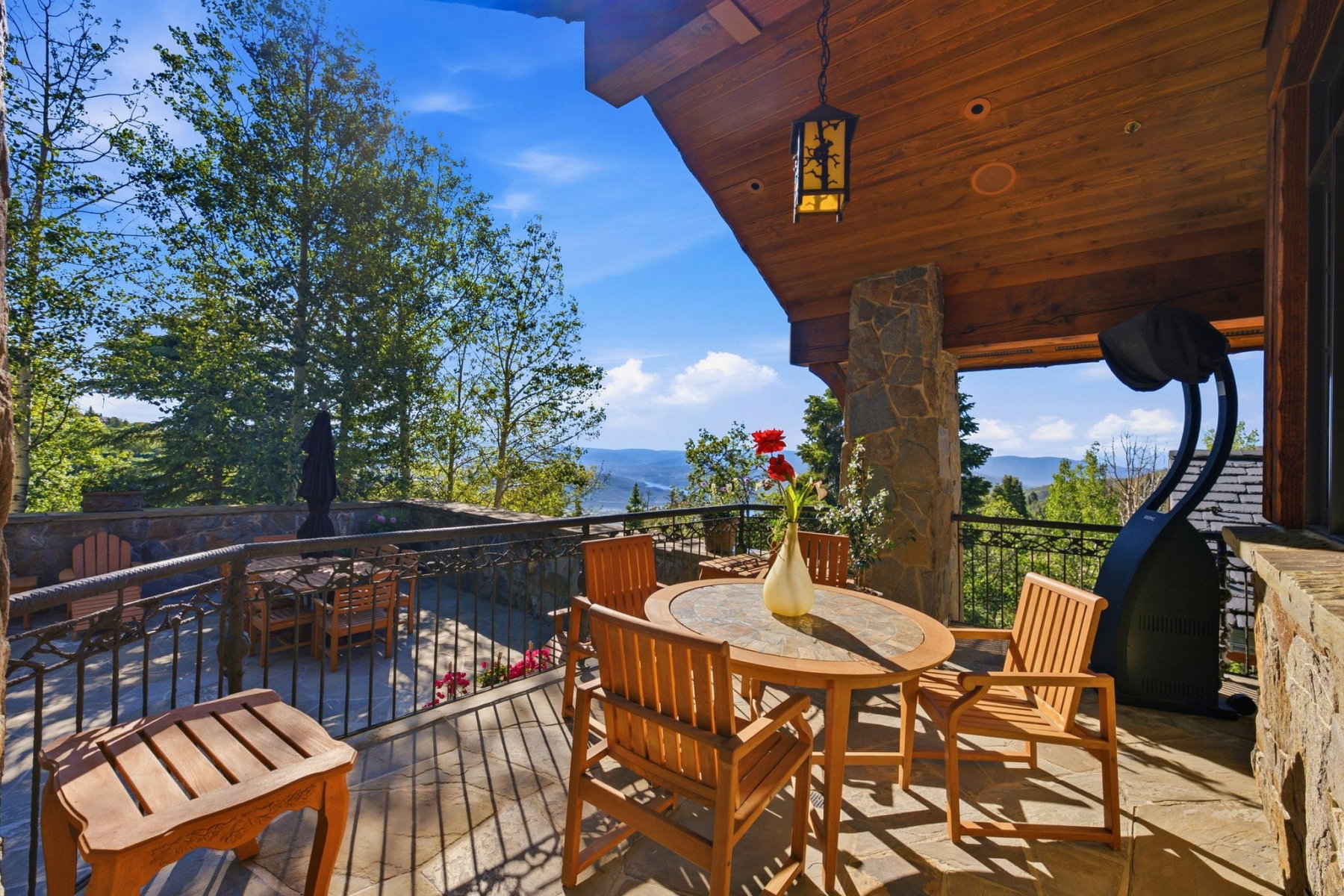 Covered outdoor patio featuring stone column supports, a wood-paneled ceiling with an attached lantern fixture, and a durable stone-tiled floor