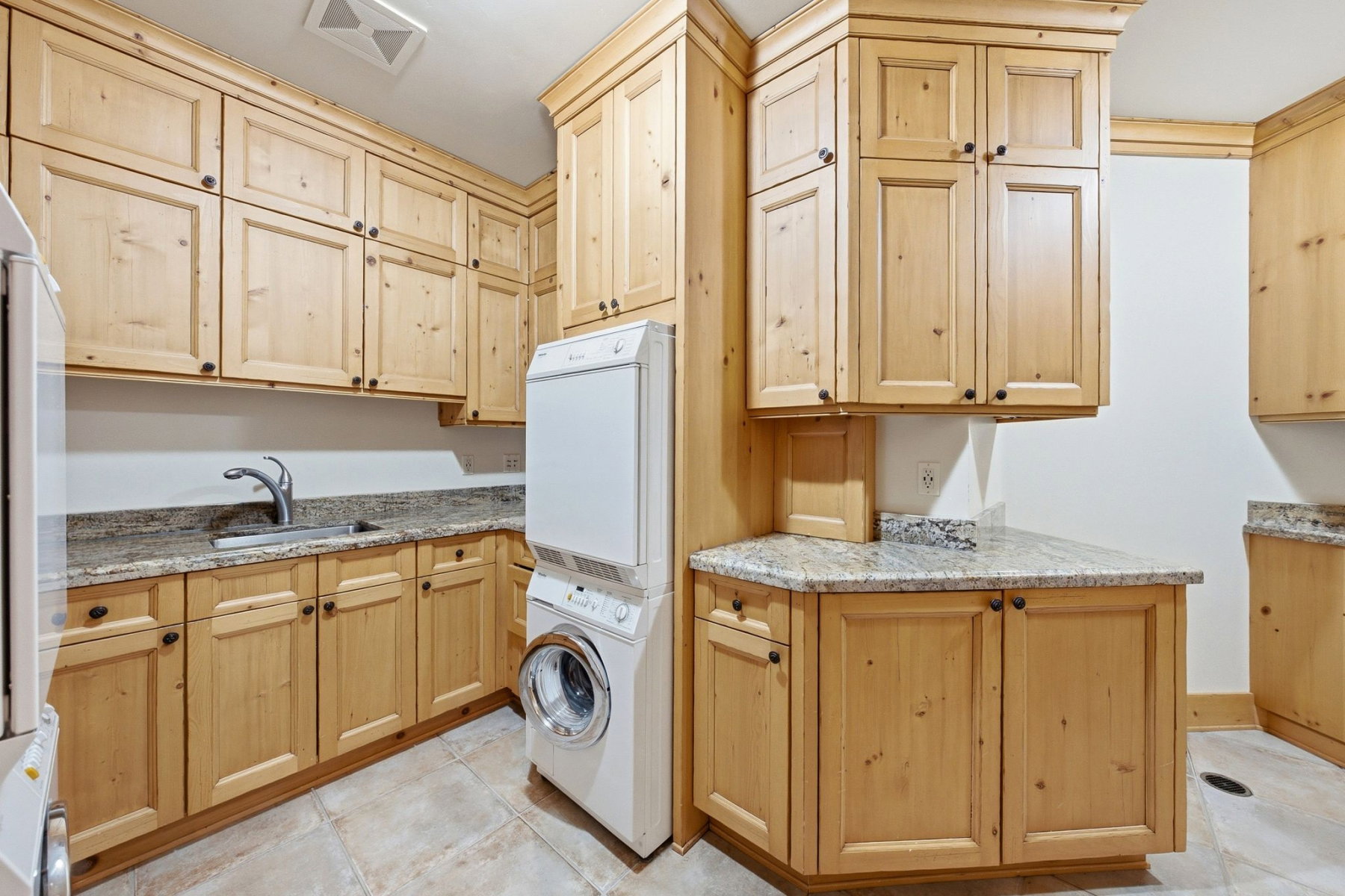 Utility room featuring extensive light wood cabinetry with dark hardware, granite countertops, a stainless steel sink with a gooseneck faucet, and tile flooring
