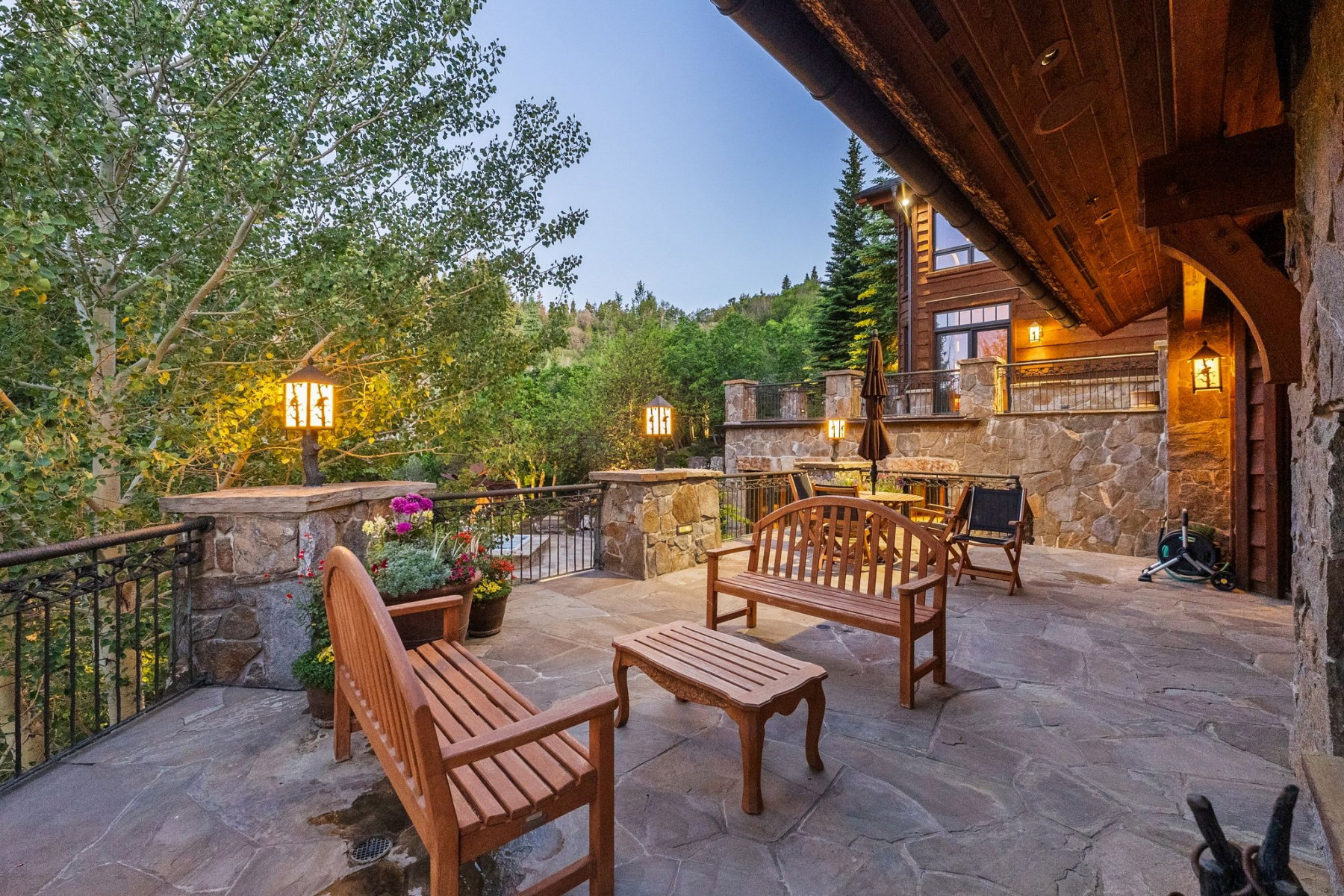 Expansive stone patio featuring a wrought iron railing, integrated stone walls, and permanent outdoor lighting fixtures