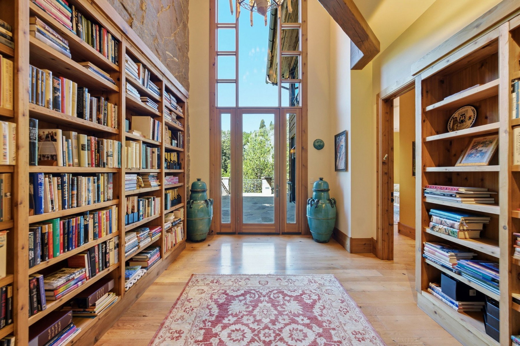 Double-height entry featuring extensive built-in wooden bookshelves, wood-finish flooring, a stone accent wall, and French doors with transom windows