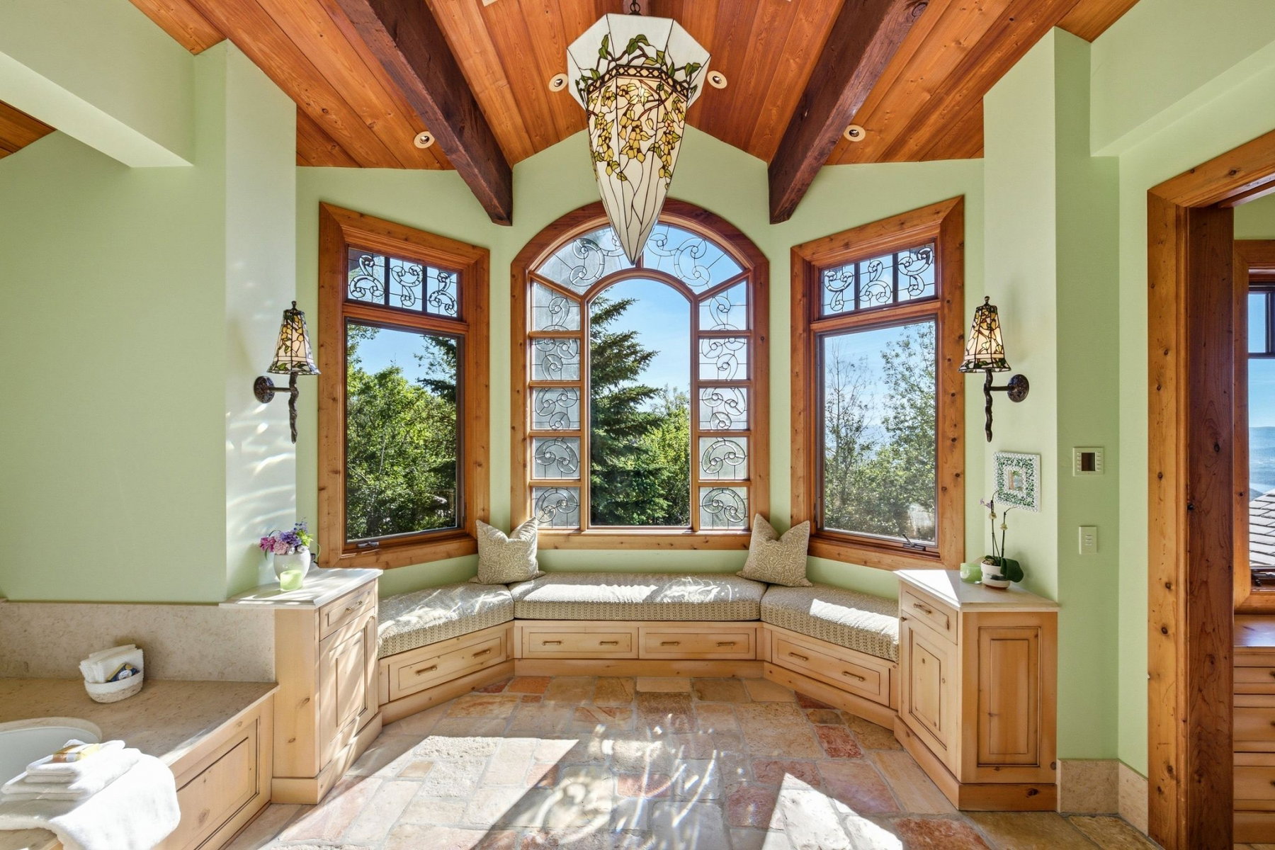 Spacious room featuring a vaulted wood-paneled ceiling with exposed beams, an arched window with decorative glasswork, and two additional windows with natural wood trim