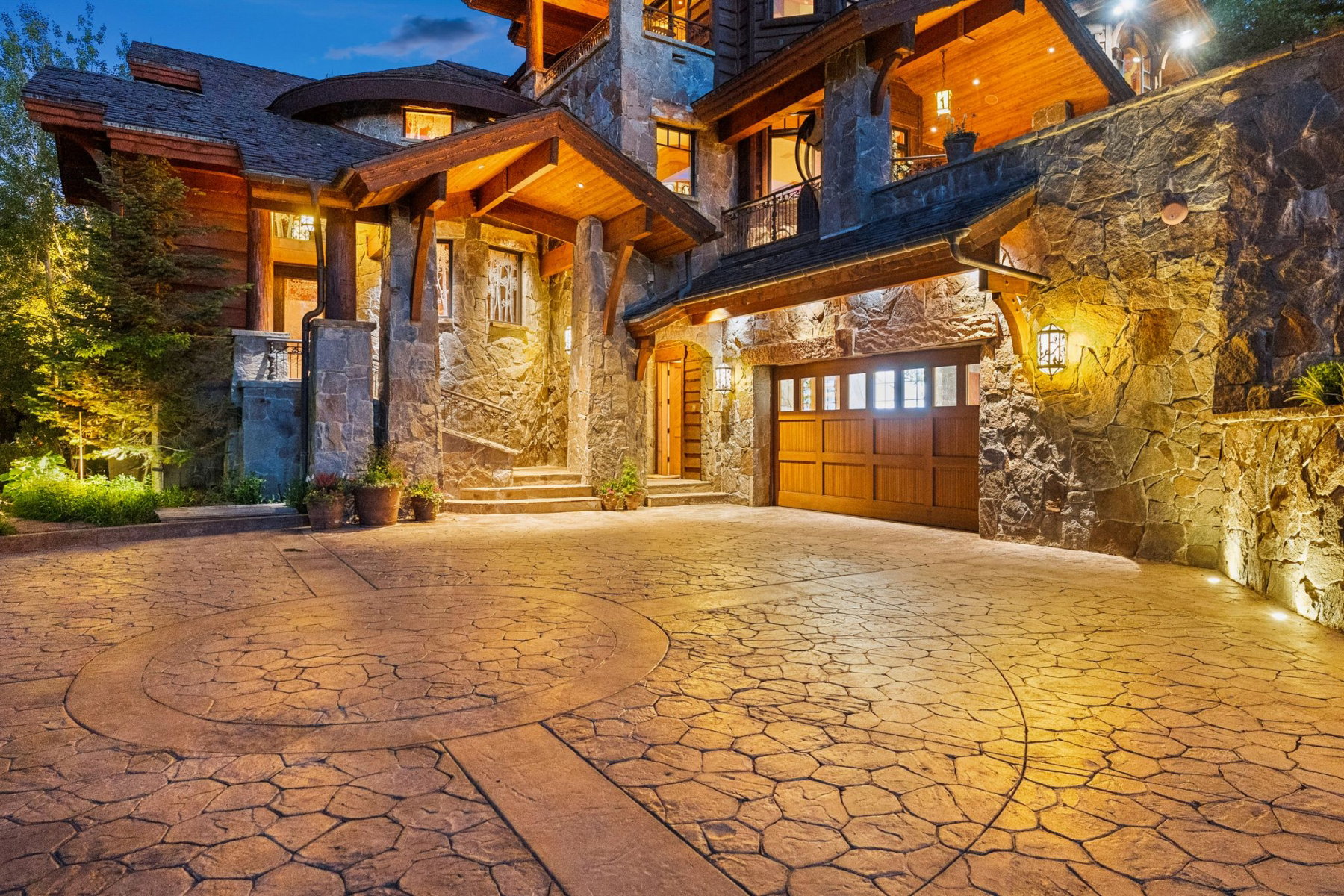 Stone-clad exterior featuring a wood garage door, stamped concrete driveway with circular detail, and exposed timber architectural elements