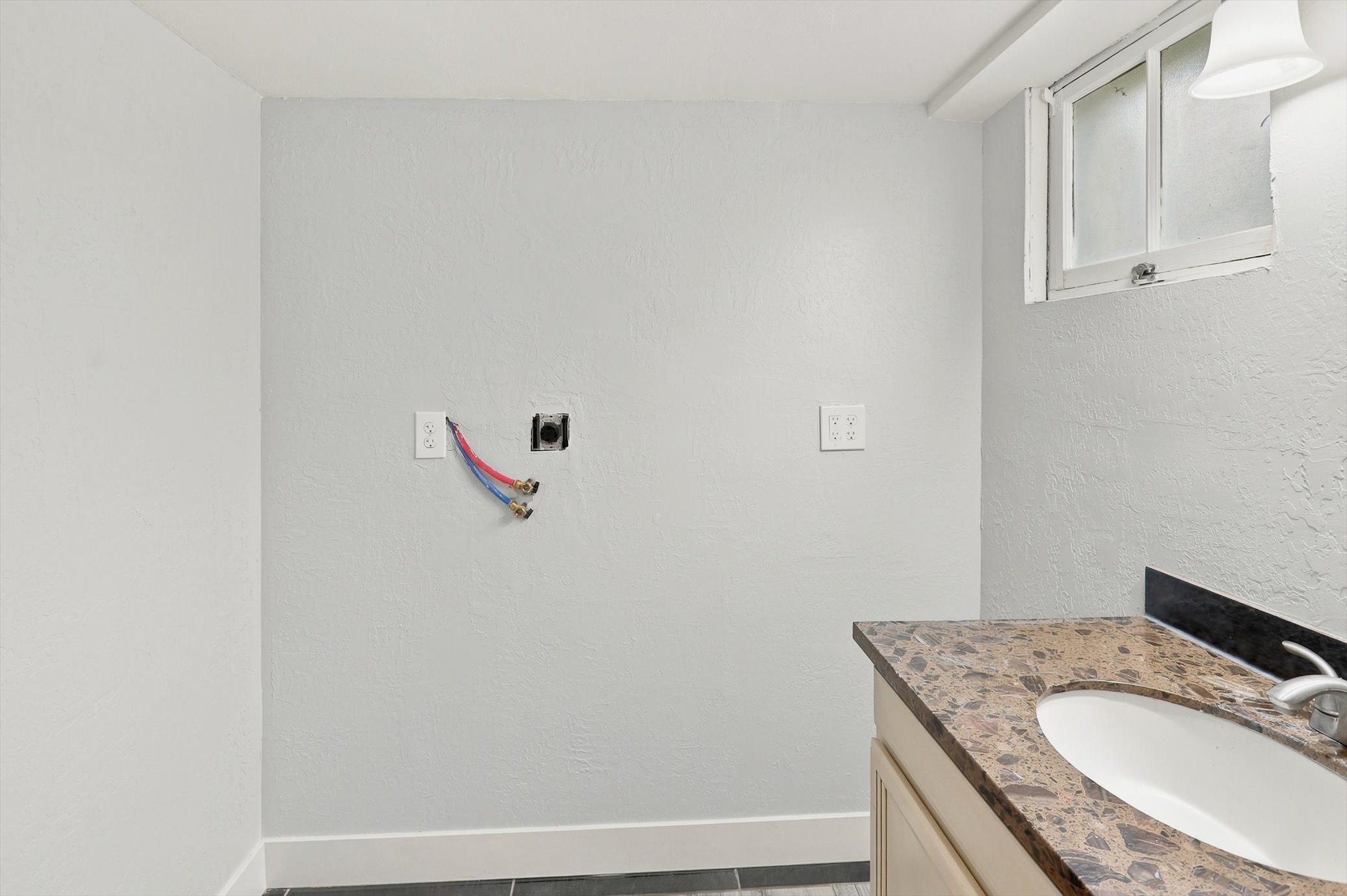 Utility area with a single-sink vanity featuring a stone-finish countertop, light wood-finish cabinetry, and a chrome faucet