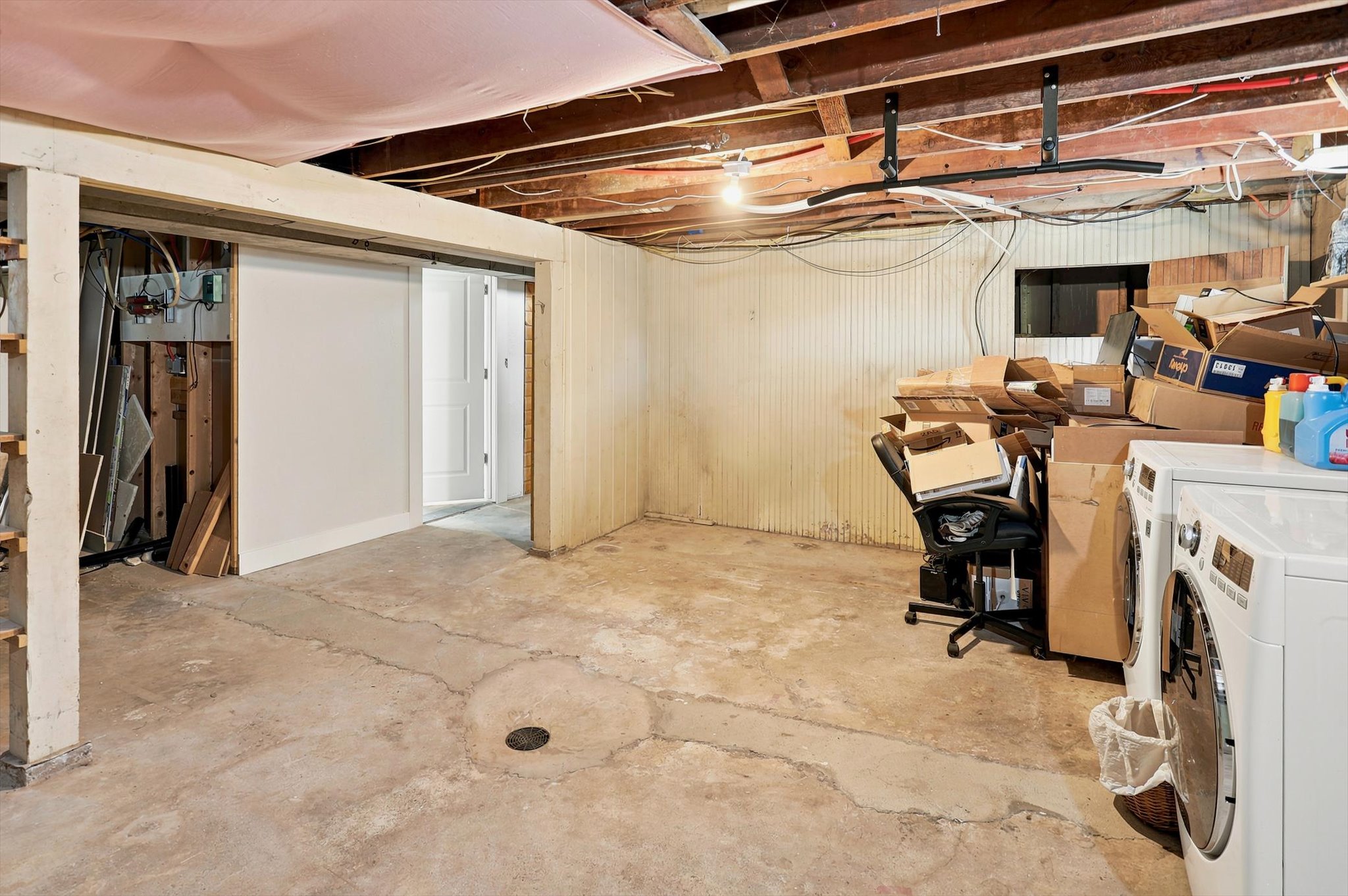Unfinished basement space featuring exposed ceiling joists, concrete flooring, and a partial wall with a sliding barn-style door