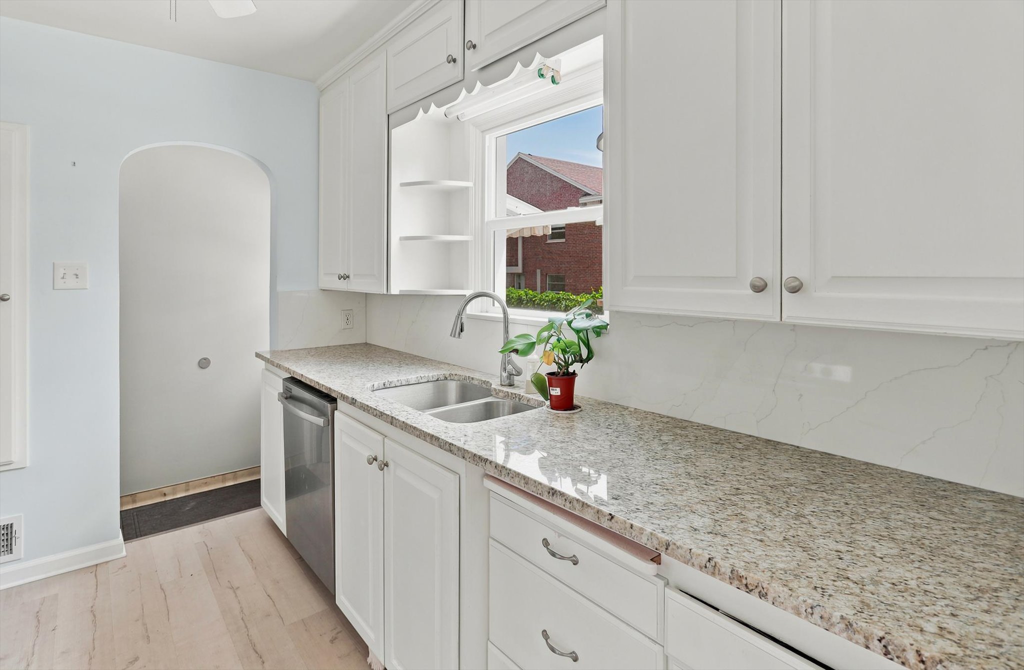 Modern kitchen featuring white shaker cabinetry, granite countertop, stainless steel double-basin sink with gooseneck faucet, and integrated dishwasher