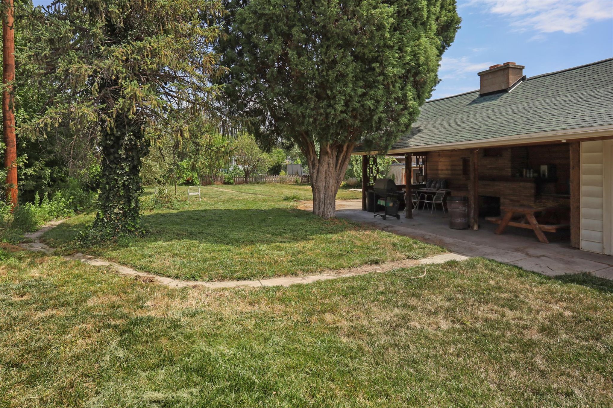 Expansive yard featuring mature trees and a covered patio with wood-paneled walls