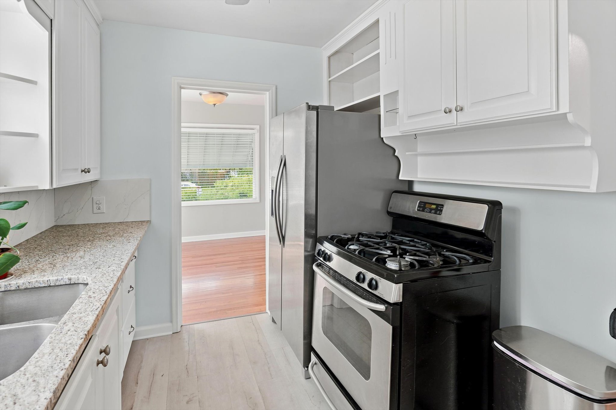 Kitchen featuring white cabinetry, granite-style countertops, stainless steel appliances, and light wood-finish flooring