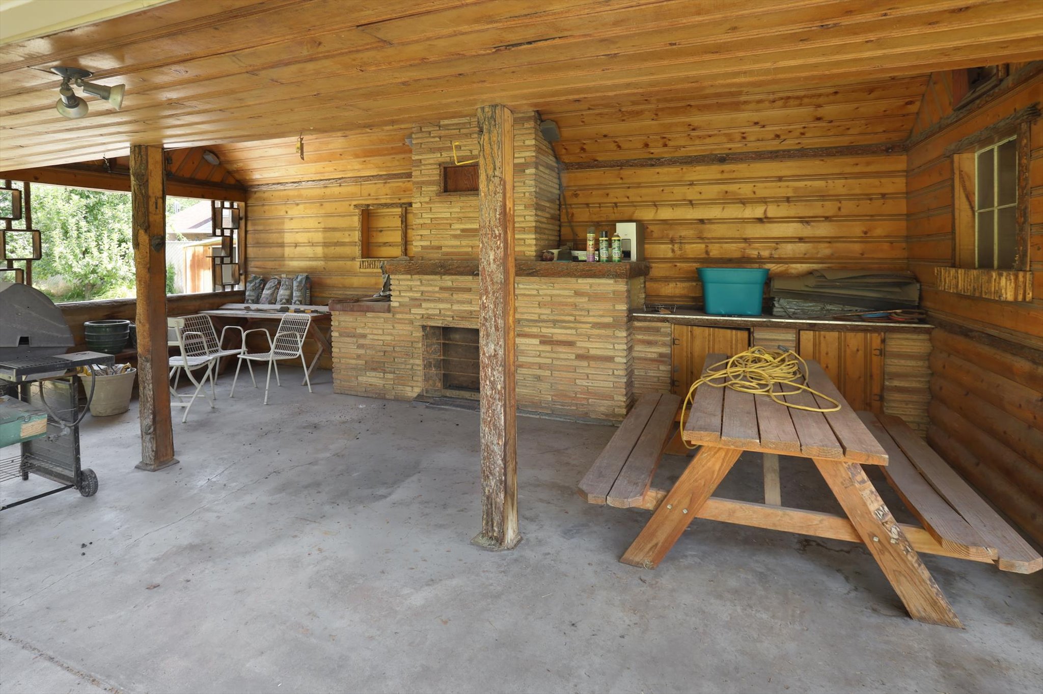 Covered patio featuring wood-paneled walls and ceiling, a concrete floor, and a built-in brick fireplace with shelving