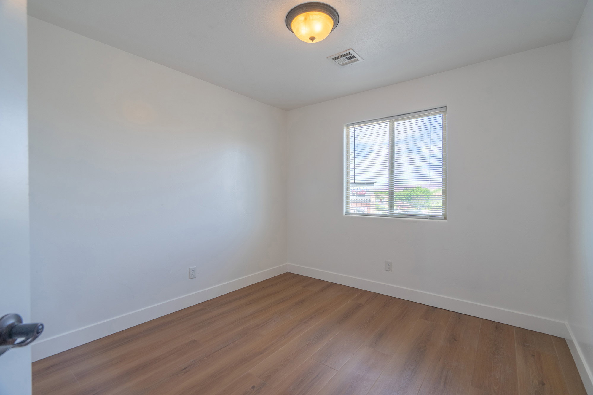 Bright interior space featuring wood-finish flooring, white walls, and a single window with blinds