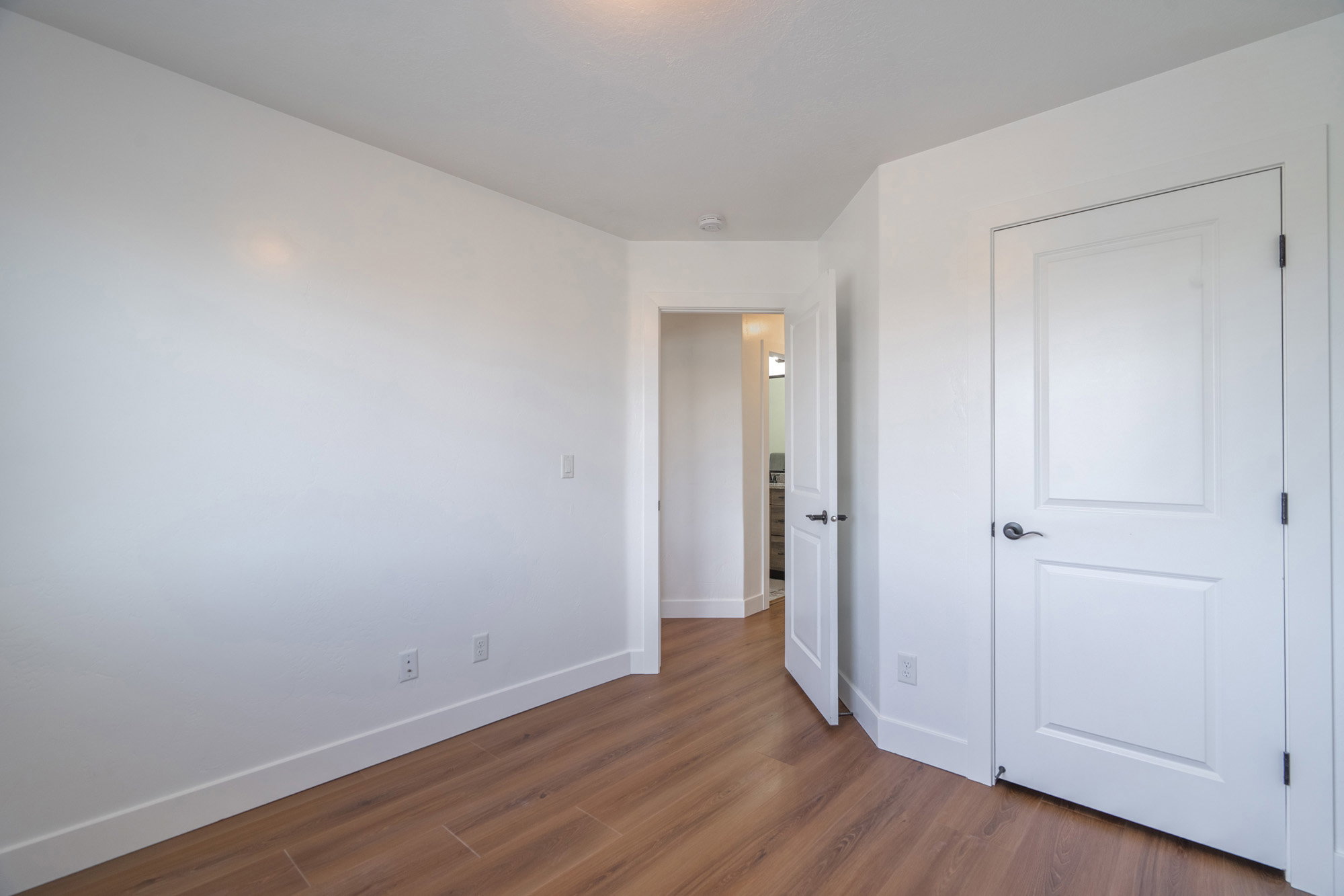 Room with wood-finish flooring, white baseboards, and bright white walls