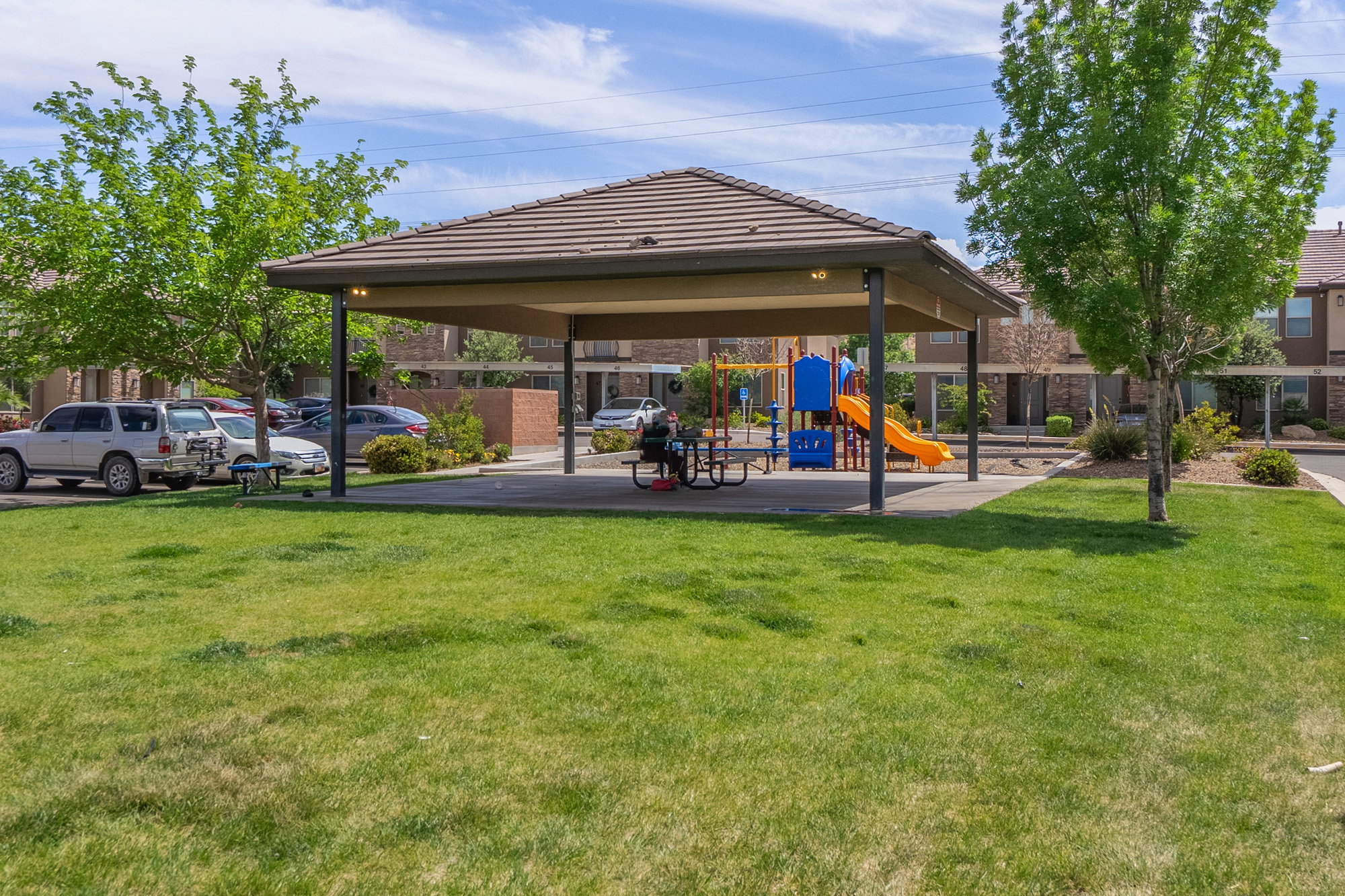 Community amenity area featuring a covered picnic structure with a tiled roof, an adjacent playground with colorful equipment, and surrounding green spaces