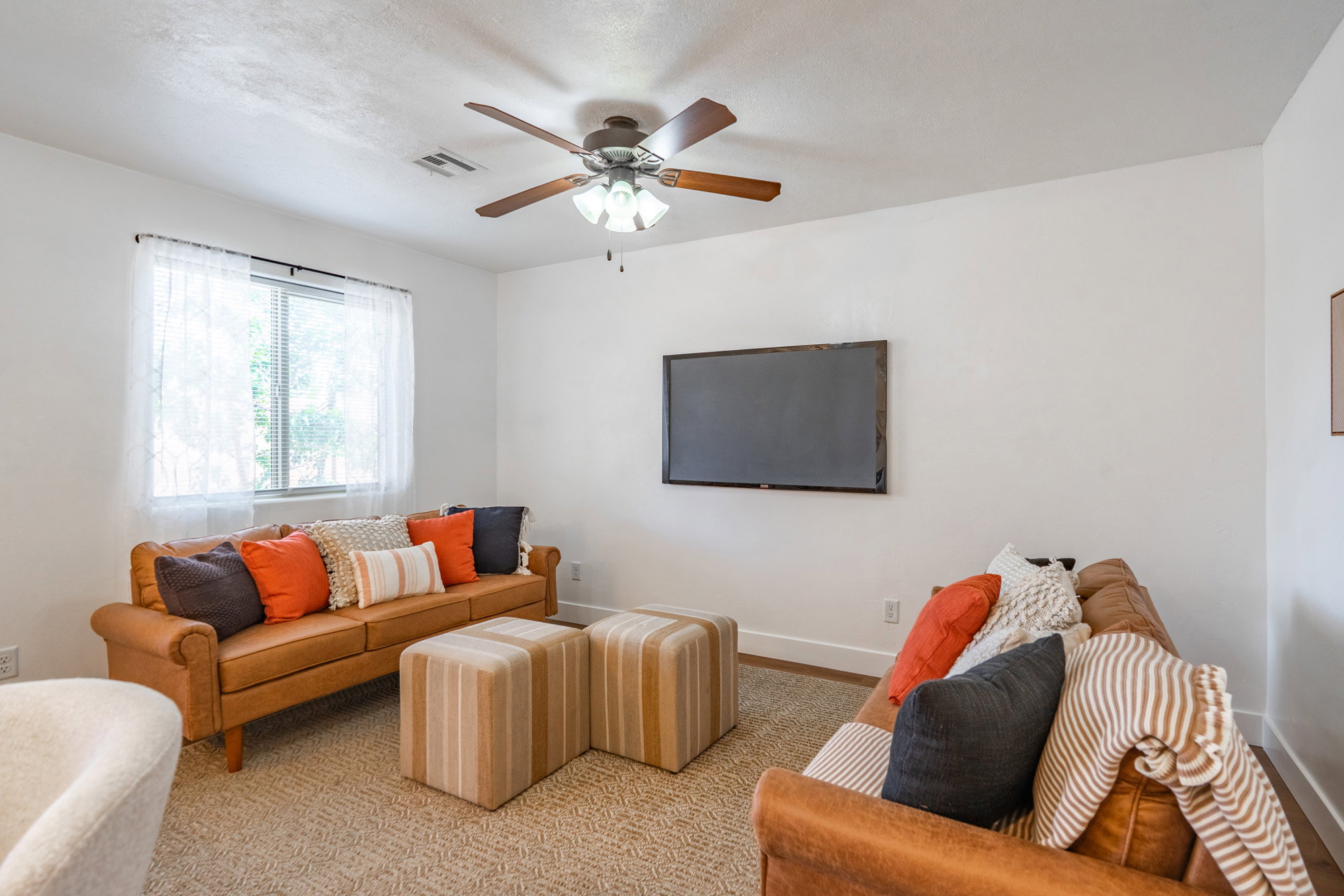 Comfortable living space featuring a ceiling fan with integrated lighting, a large window, white walls, and light-toned patterned carpeting