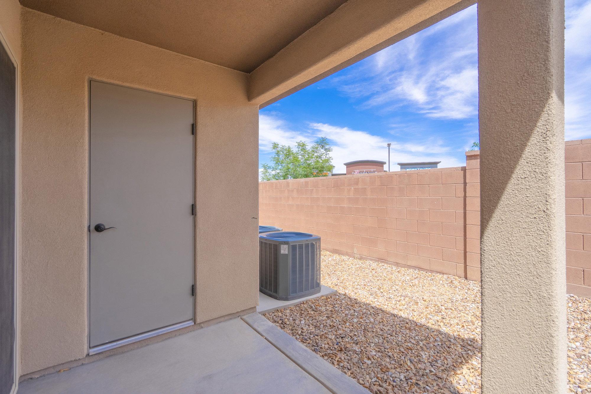 Covered patio with textured stucco finishes, concrete flooring, and an exterior storage door