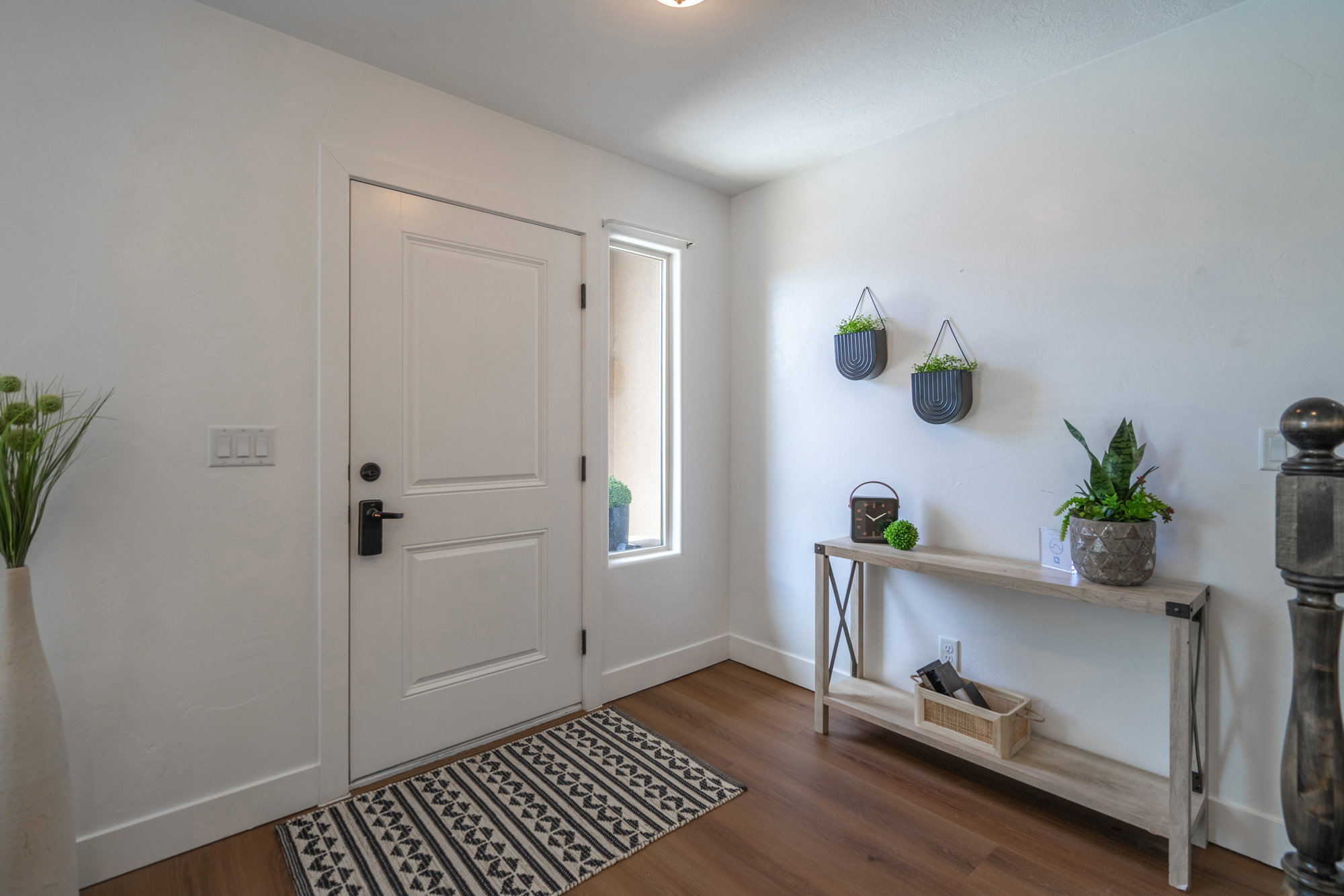 Bright entryway featuring a solid-panel door with matte black hardware, wood-finish flooring, a sidelight window, and crisp white walls