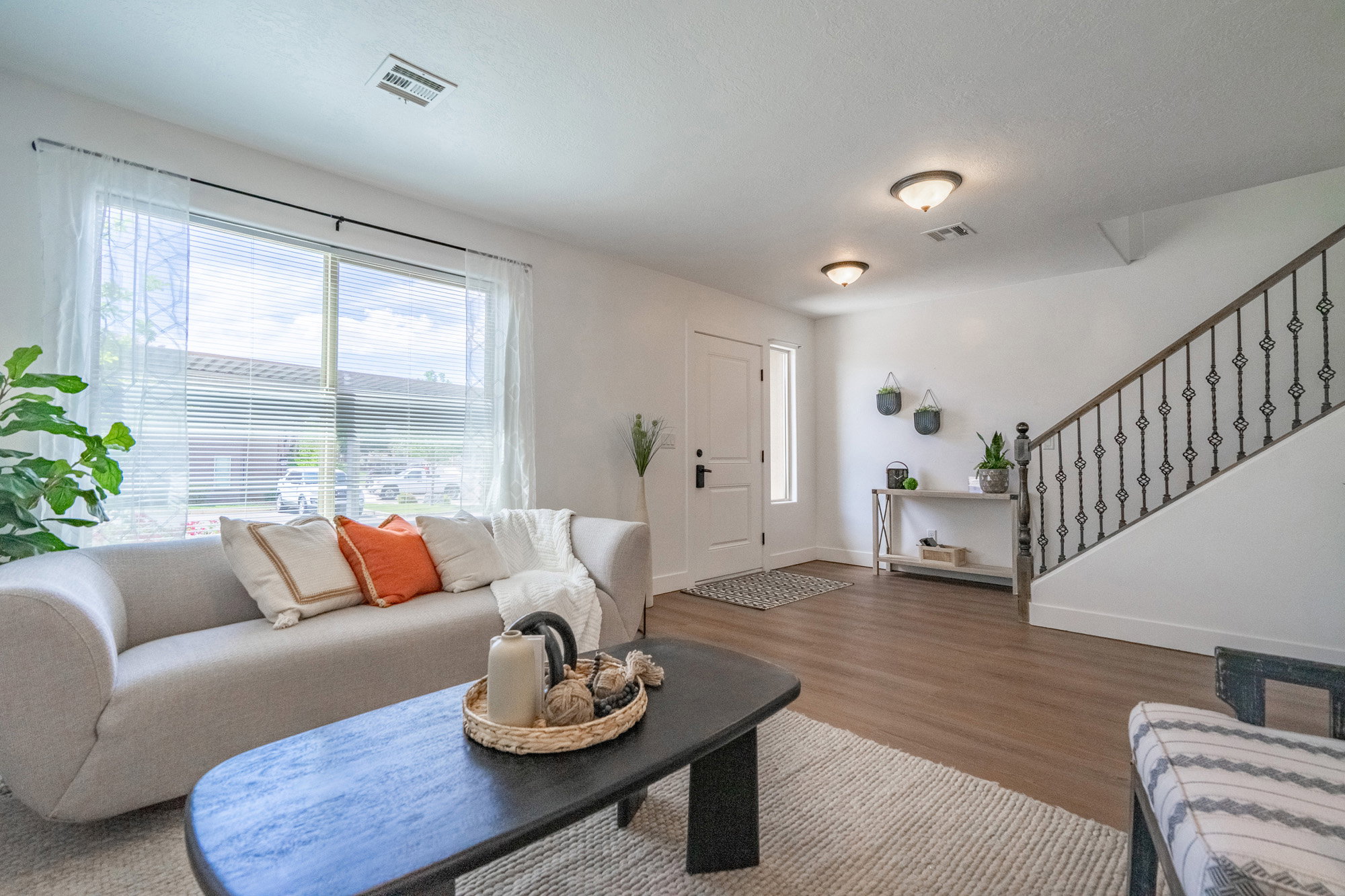 Open-concept living space featuring wood-finish flooring, a white front door with a sidelight, and a staircase with decorative iron spindles and a dark wood handrail