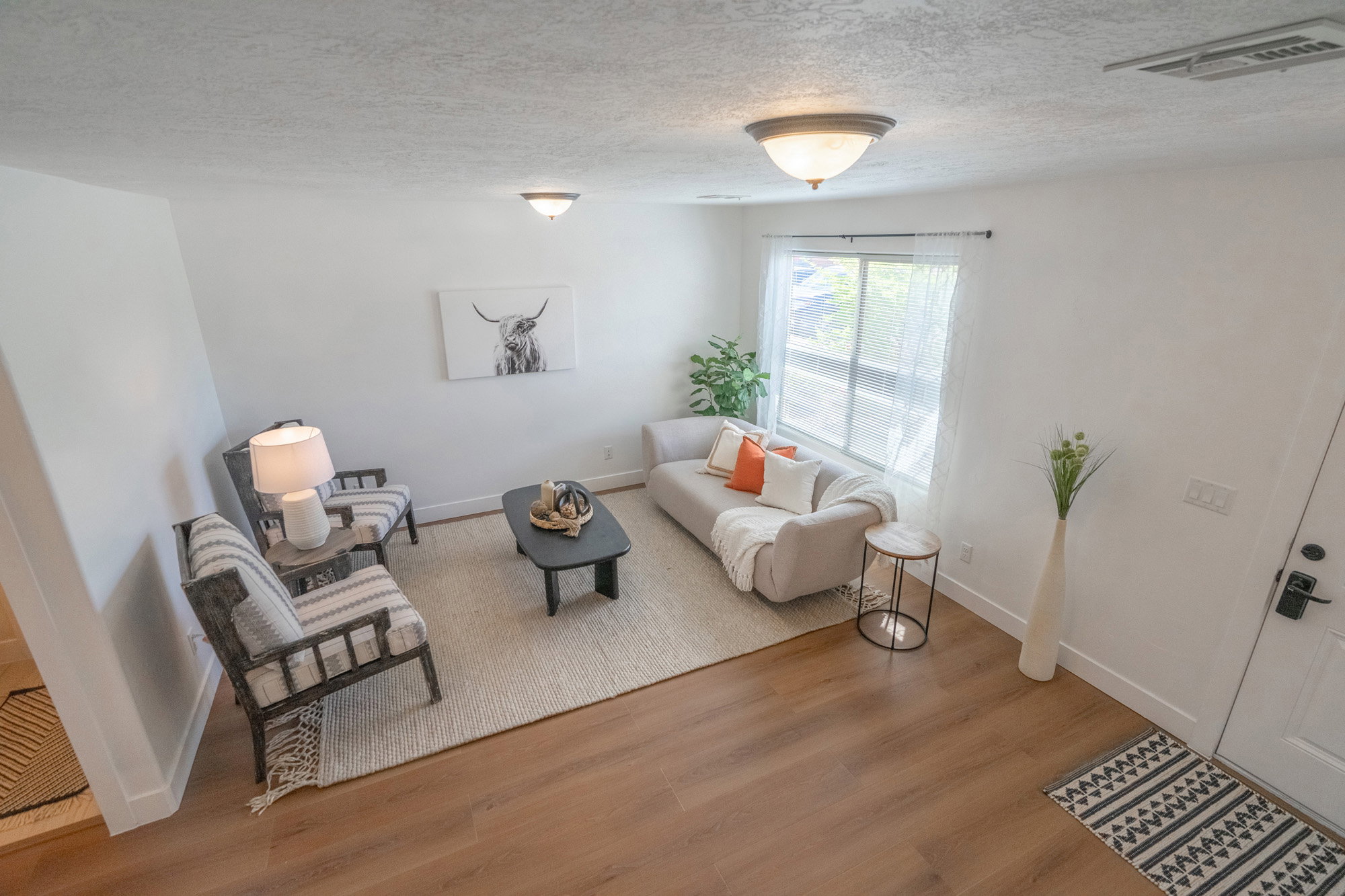 Bright living area featuring wood-finish flooring, white walls, and a large window providing ample natural light