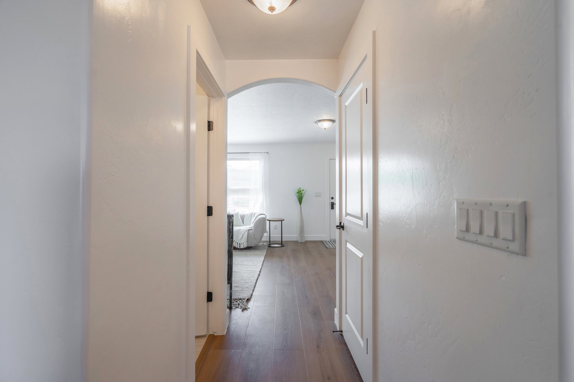 Hallway featuring wood-finish flooring, white paneled doors, an arched doorway, and overhead lighting fixtures