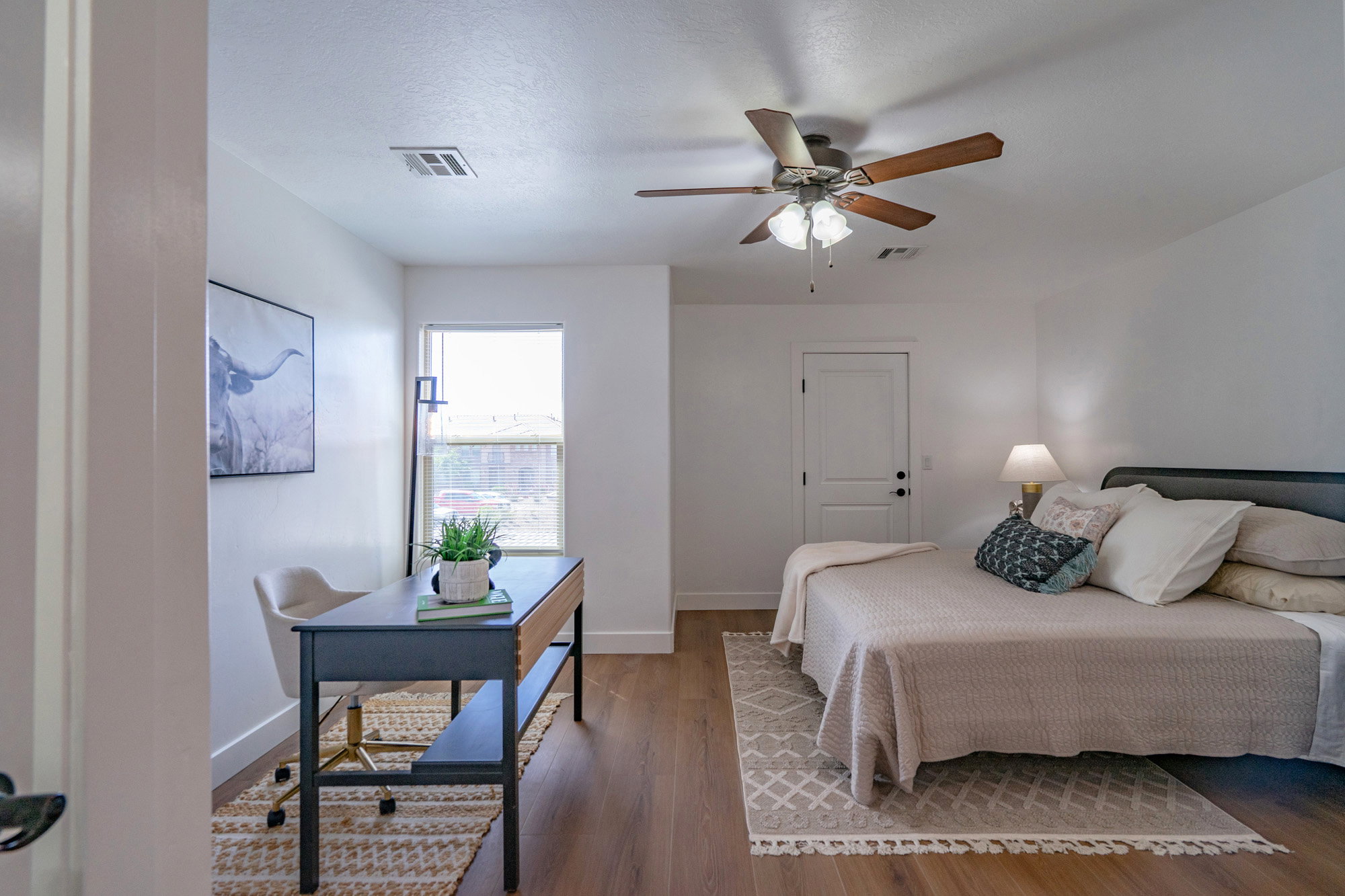 Bright room featuring wood-finish flooring, a ceiling fan with light fixture, white walls, a white door, and a single window