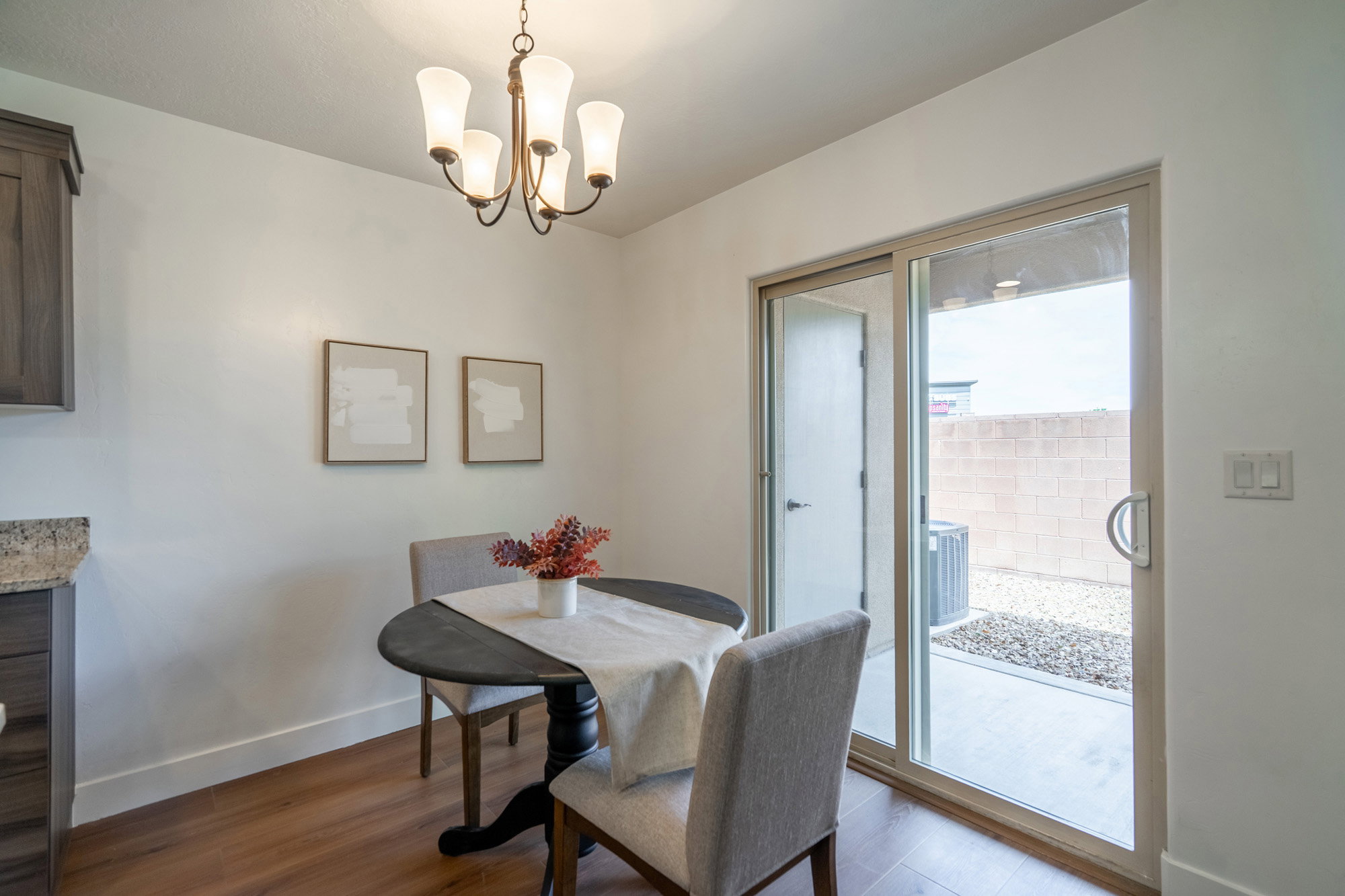 Dining area featuring wood-finish flooring, a contemporary chandelier, and a sliding glass door to an outdoor patio with a gravel landscape and block wall
