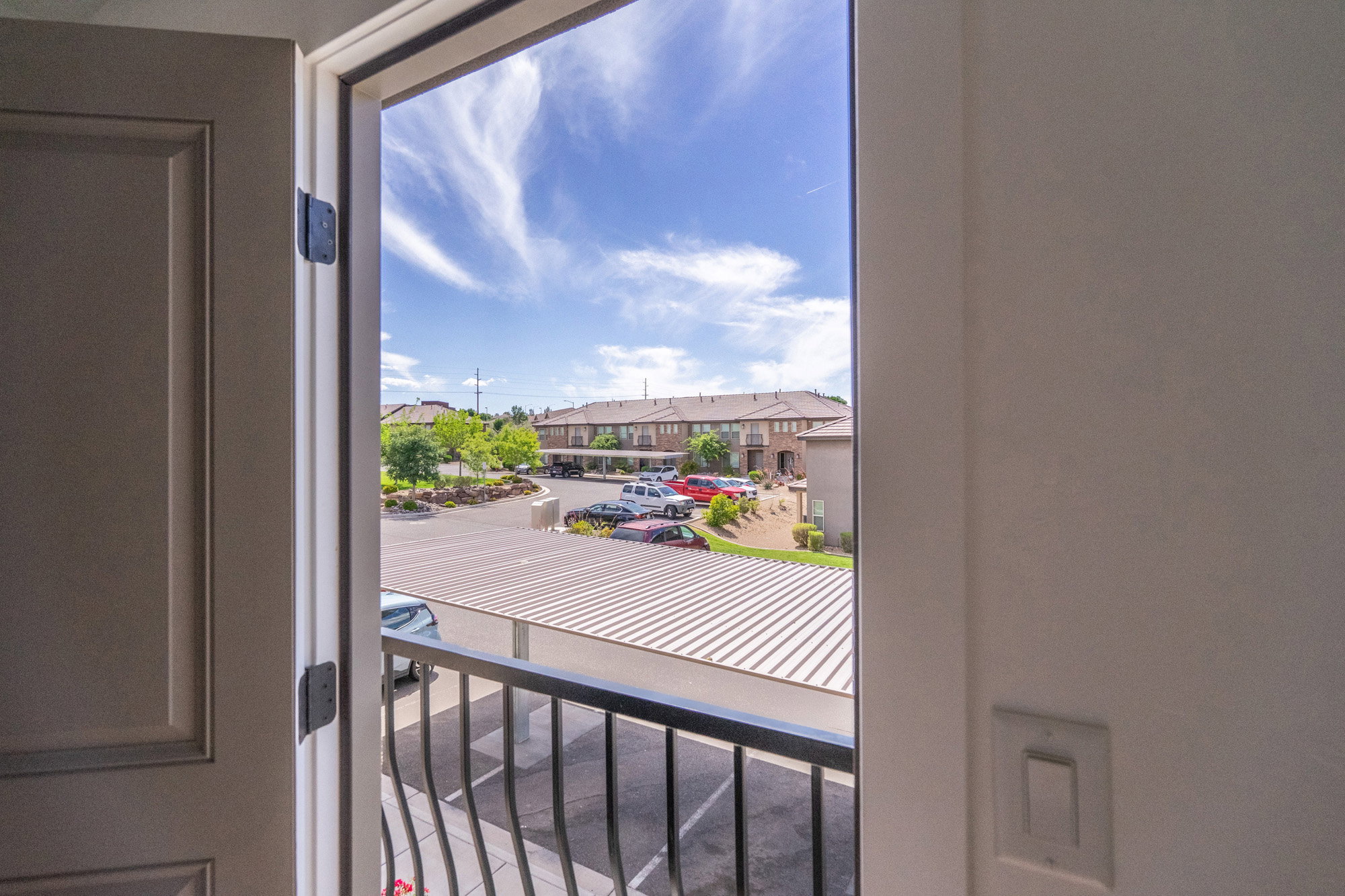 Balcony with black wrought iron railing overlooking a paved parking area and multi-level residential structures