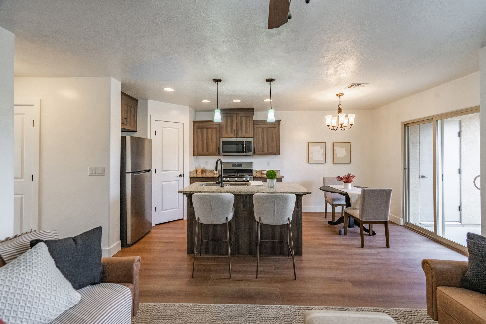 Open-concept living area featuring wood-finish flooring, a kitchen island with pendant lighting, stainless steel appliances, and sliding glass doors to outdoor space