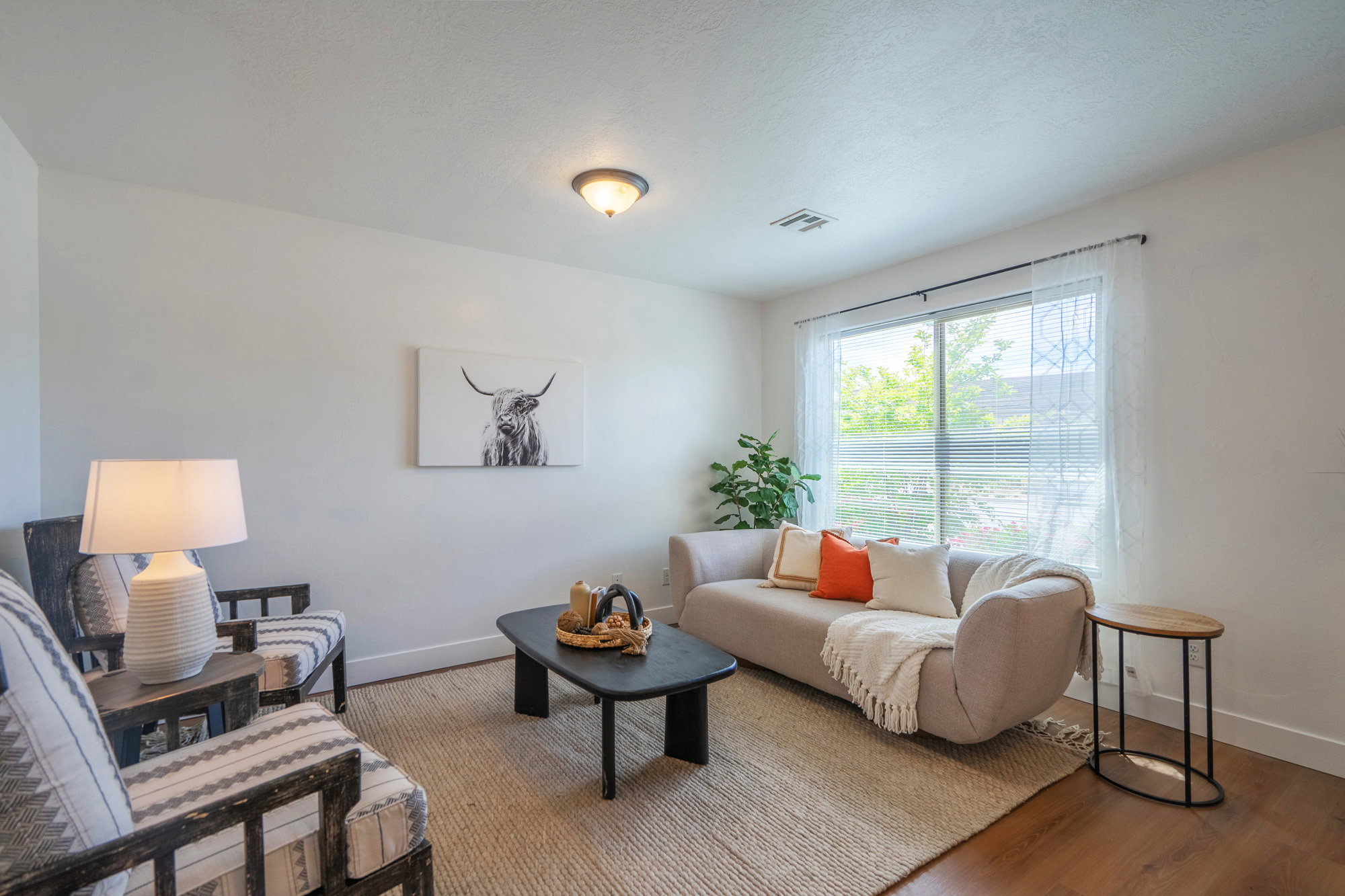 Bright living area featuring a large window with white blinds and sheer curtains, wood-finish flooring, recessed lighting, and a neutral color palette